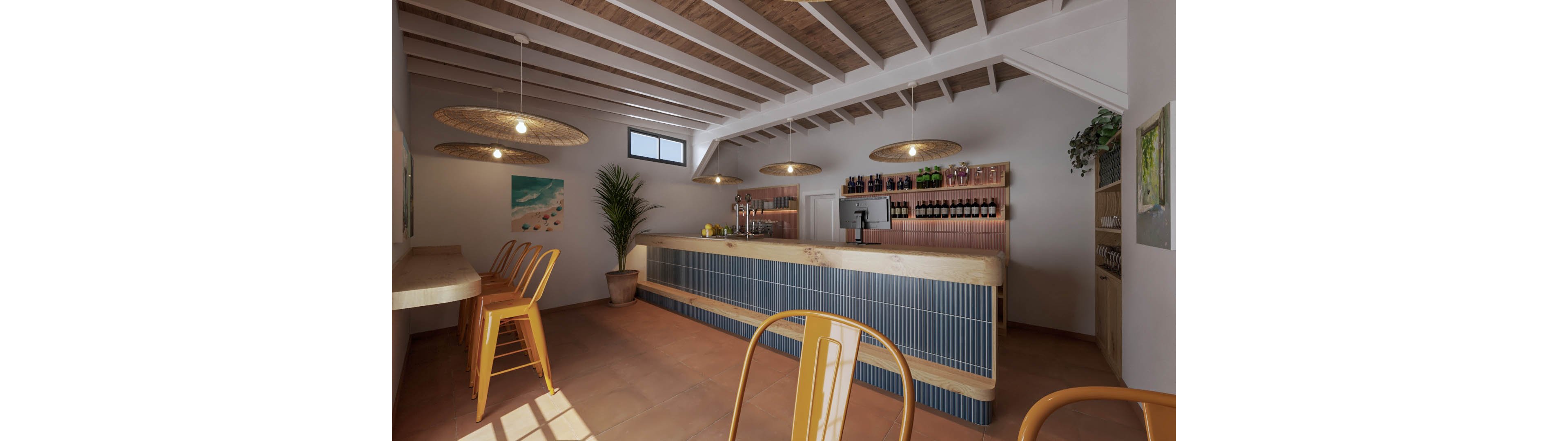 A contemporary bar interior features a long wooden counter with blue paneling and bar stools in the foreground. Warm pendant lights hang from a white beamed ceiling, casting soft light across the terracotta floor. Bottles and glassware are neatly arranged on shelves behind the bar alongside a point-of-sale screen. A potted plant, wall art, and a small high-top seating area add to the relaxed, coastal-inspired atmosphere.
