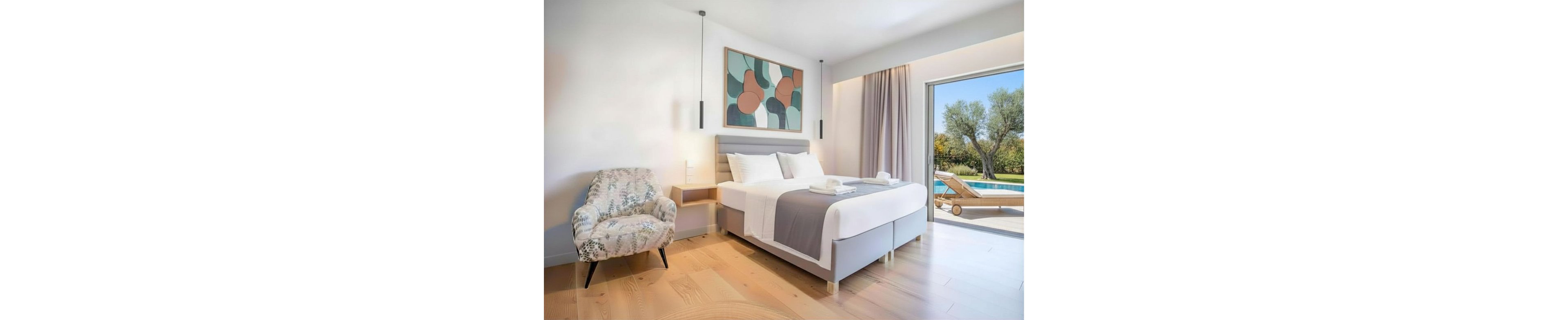 A contemporary bedroom features a neatly made double bed with white linens and a gray runner. A patterned armchair sits beside the bed, while minimalist pendant lights hang from the ceiling. Large sliding glass doors open to a terrace with sun loungers and a swimming pool, overlooking a green garden with trees. Soft neutral tones and natural light create a calm, inviting atmosphere.