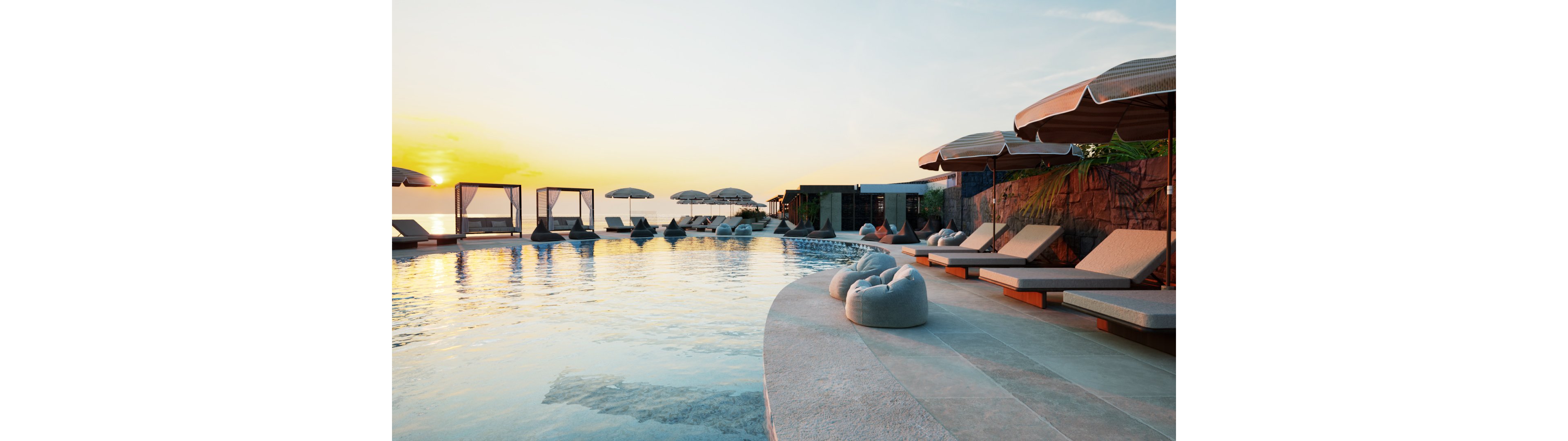 A tranquil infinity pool overlooks the ocean at sunset, with soft golden light reflecting on the calm water. Modern sun loungers and shaded cabanas line the curved poolside deck, creating a luxurious resort atmosphere. Neutral tones of beige and stone contrast with the warm sky, while a few scattered cushions add comfort and relaxation. The scene evokes a peaceful vacation mood in an upscale coastal setting.