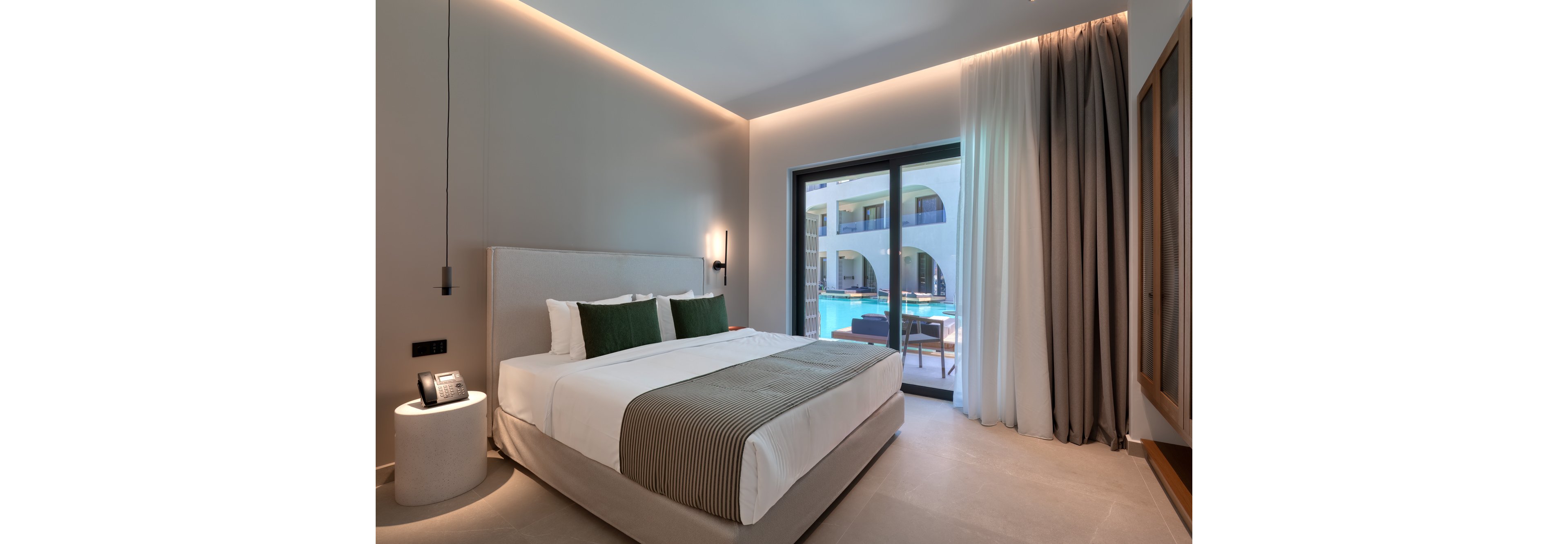 Contemporary hotel room with a large bed faces a glass door opening to a poolside courtyard. Neutral walls and flooring are accented by green cushions and a striped bed runner. Soft ambient lighting, sheer and blackout curtains, and a bedside table with a phone create a calm, upscale atmosphere. The view through the sliding door shows sunlit balconies and the blue water of the swimming pool.
