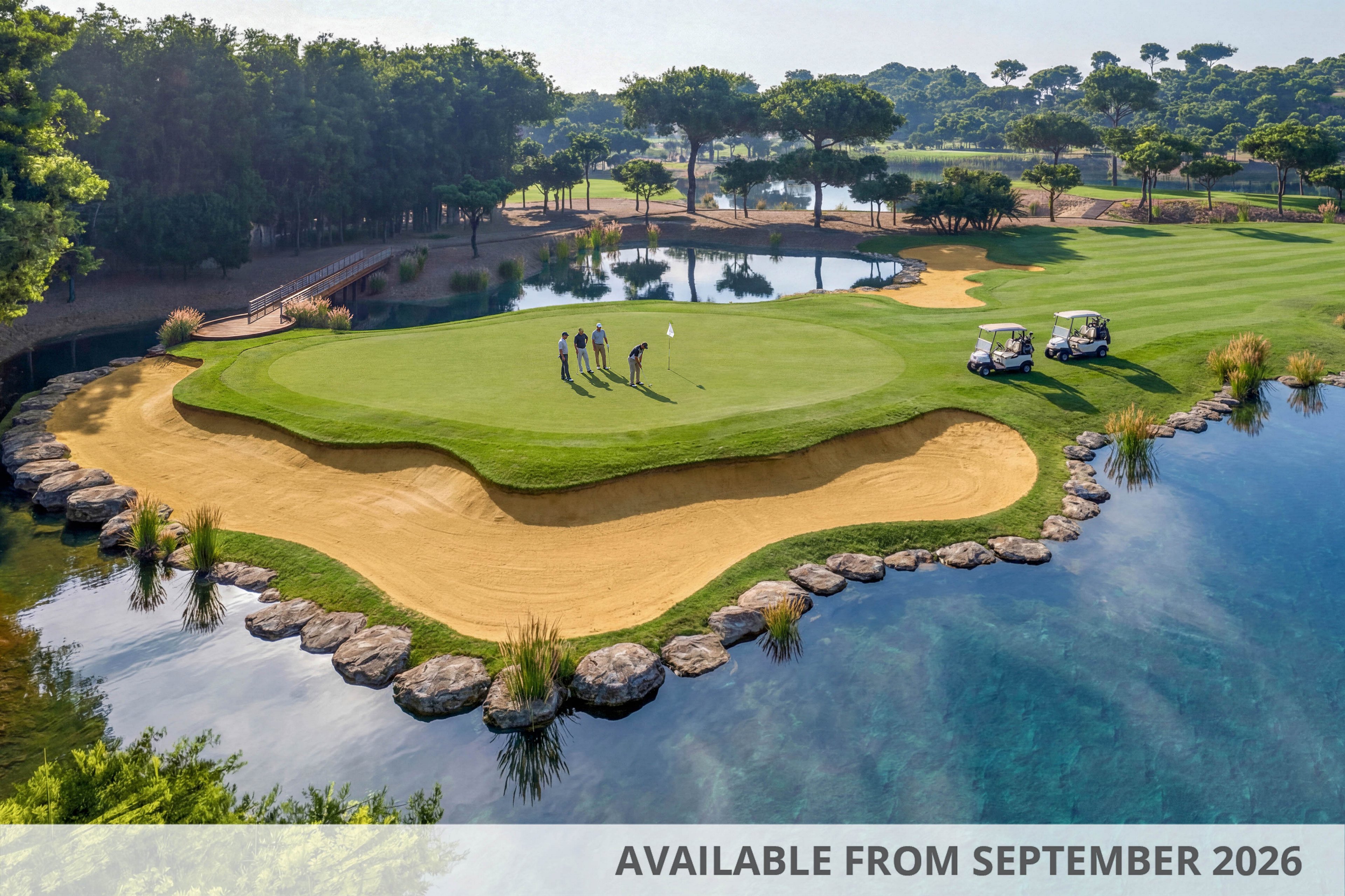 A group of golfers stands on a lush island green surrounded by sand bunkers and clear blue water. Two golf carts are parked nearby on the manicured fairway. The course is bordered by dense trees and reflective ponds under a bright sky. The elevated aerial view highlights the dramatic shoreline, curved bunkers, and serene resort-like landscape.