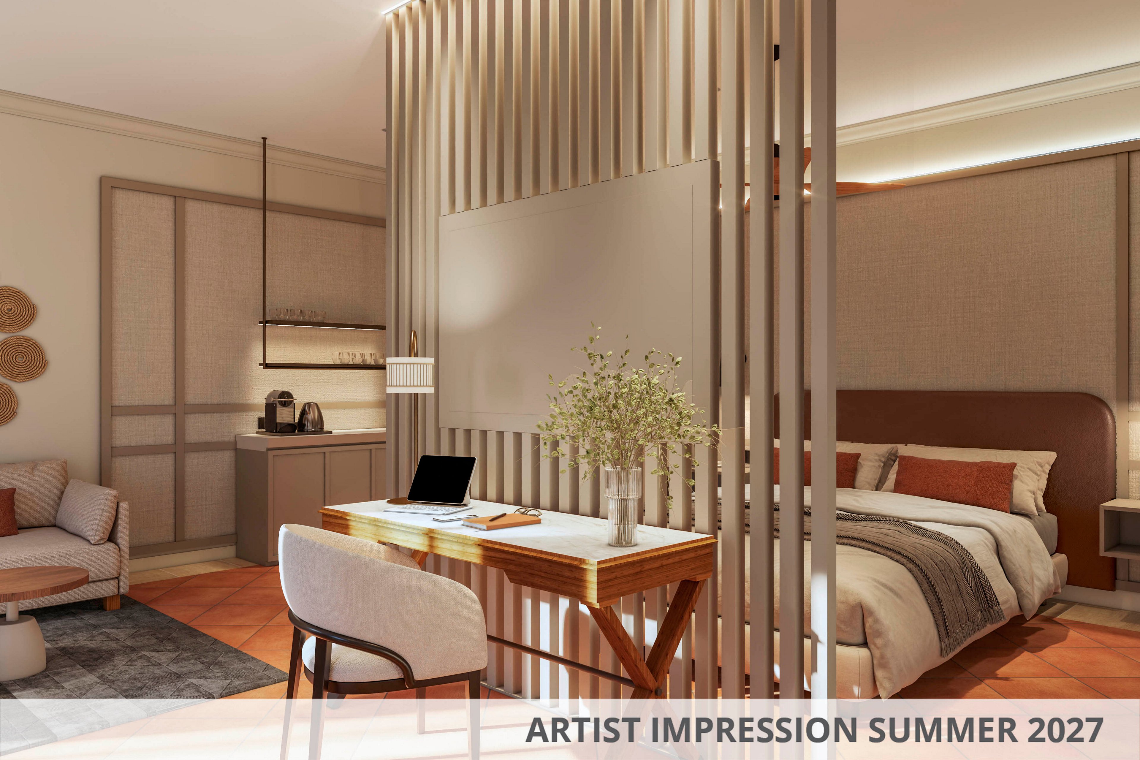 Rendered interior of a contemporary studio bedroom with a wooden desk and chair in the foreground. A cozy bed with layered pillows and blankets sits behind vertical slatted room dividers. Soft, warm lighting highlights neutral tones, minimalist furniture, and a small seating area with armchair and side table. A kitchenette with coffee machine and storage cabinets appears in the background. Text on the image reads ARTIST IMPRESSION SUMMER 2027.