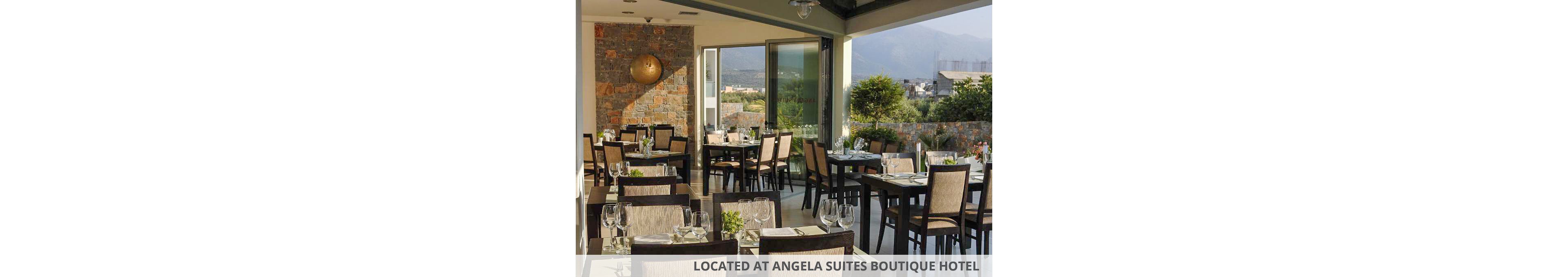 A contemporary restaurant dining area is set with neatly arranged tables and chairs. Each table is prepared with glassware, cutlery, and small green centerpieces, ready for guests. Large windows and open doors reveal a terrace and distant mountains under a clear sky. Warm natural light fills the space, highlighting stone walls and modern decor for an inviting atmosphere.