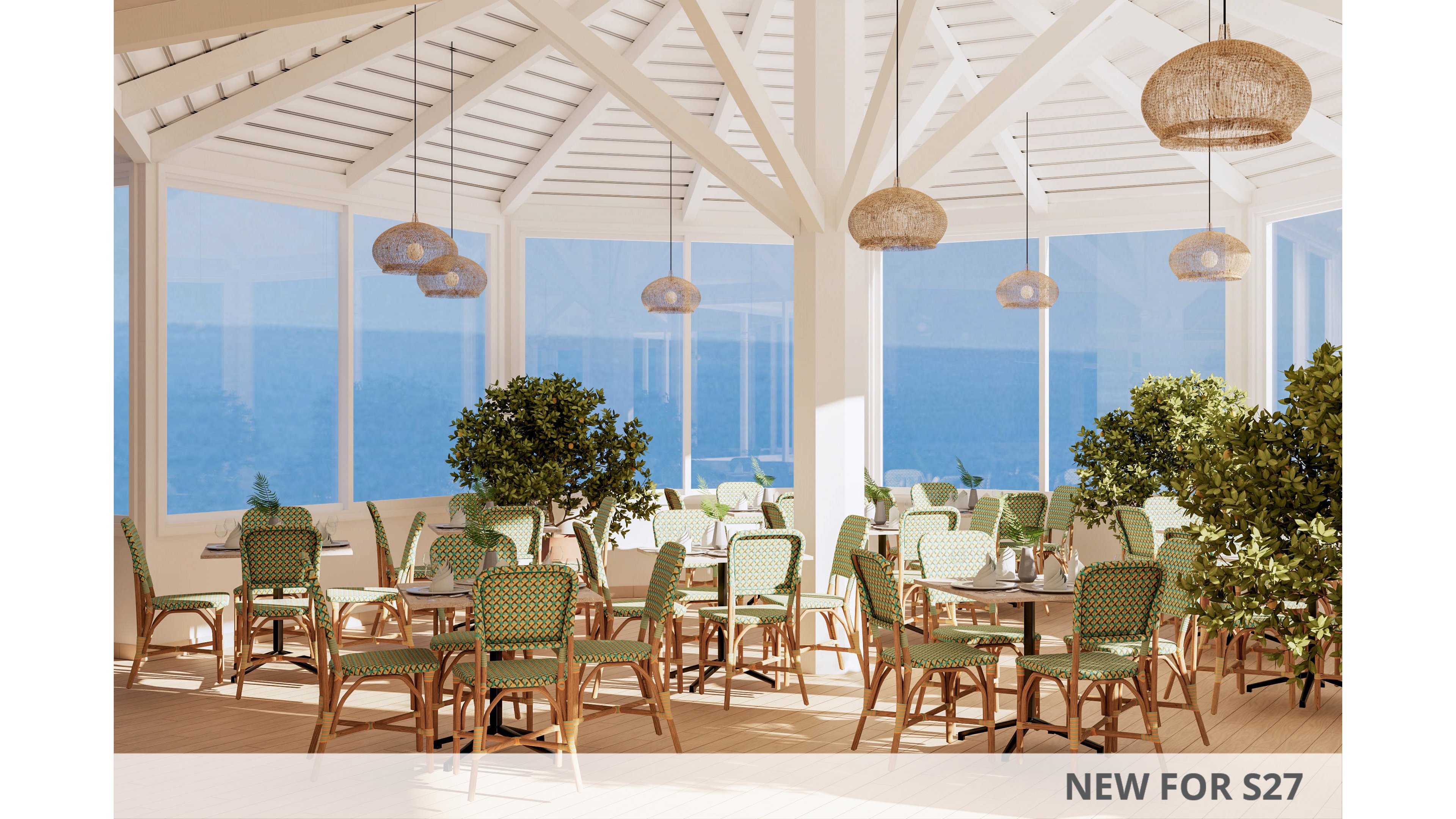 Sunlit dining area features wicker chairs and round tables arranged in a spacious coastal restaurant. Large floor-to-ceiling windows reveal a clear view of the blue ocean outside. Green potted plants and woven pendant lights add natural texture and warmth to the white wooden interior. The atmosphere feels airy, relaxed, and inviting for seaside meals.