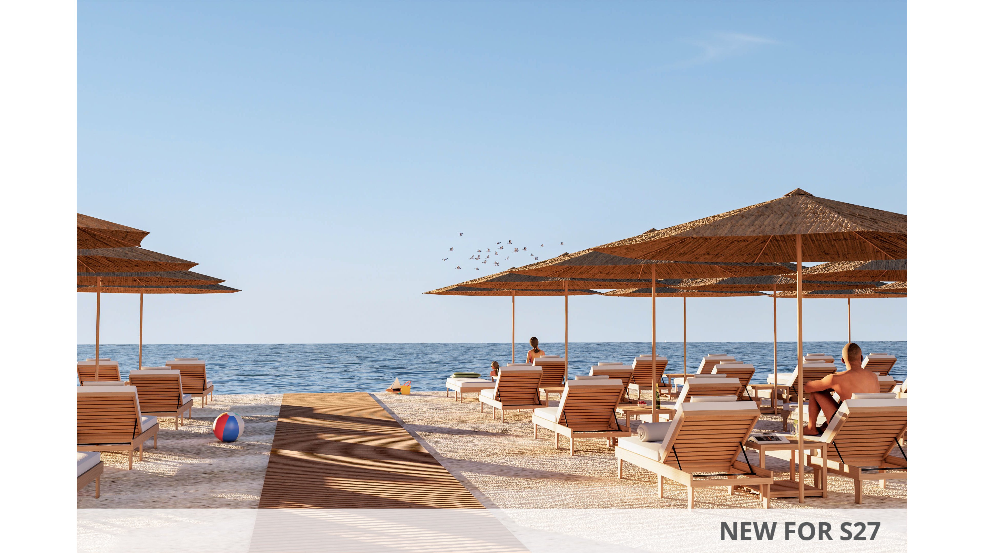 A tranquil beach resort features rows of wooden lounge chairs under wide straw umbrellas facing the calm sea. A wooden walkway leads from the foreground toward the water, guiding the eye to the horizon. A few people relax on the chairs while others stand near the shoreline, enjoying the clear weather. The scene is bathed in warm sunlight with a clear blue sky and gentle waves in the background.