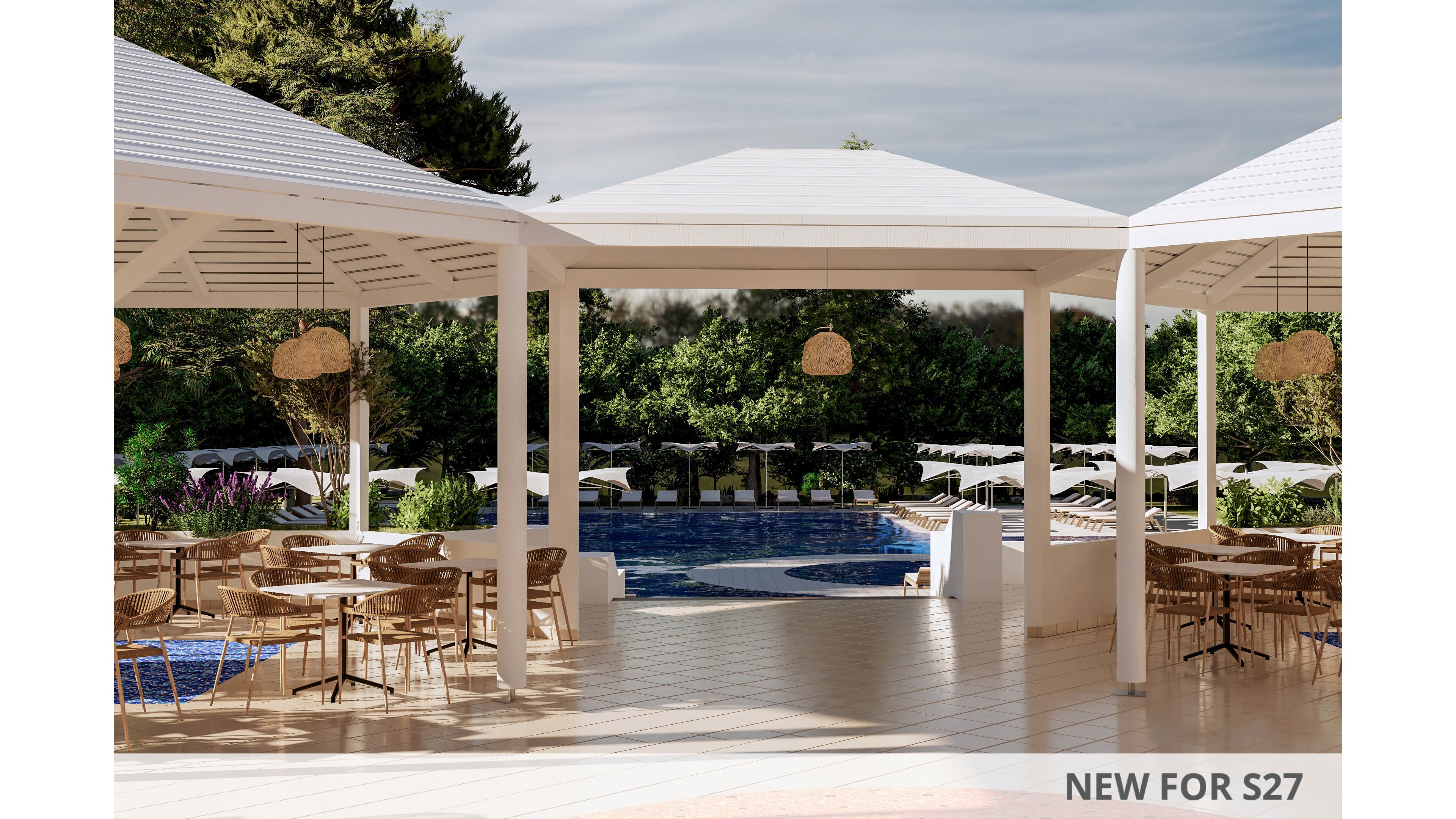 Open-air white pavilions frame a view of a resort swimming pool. Wooden tables and chairs are arranged on a tiled terrace, suggesting an outdoor dining or lounge area. Sun loungers and umbrellas line the pool in the background, surrounded by lush greenery and trees. Warm sunlight and neutral tones create a relaxed, vacation atmosphere.