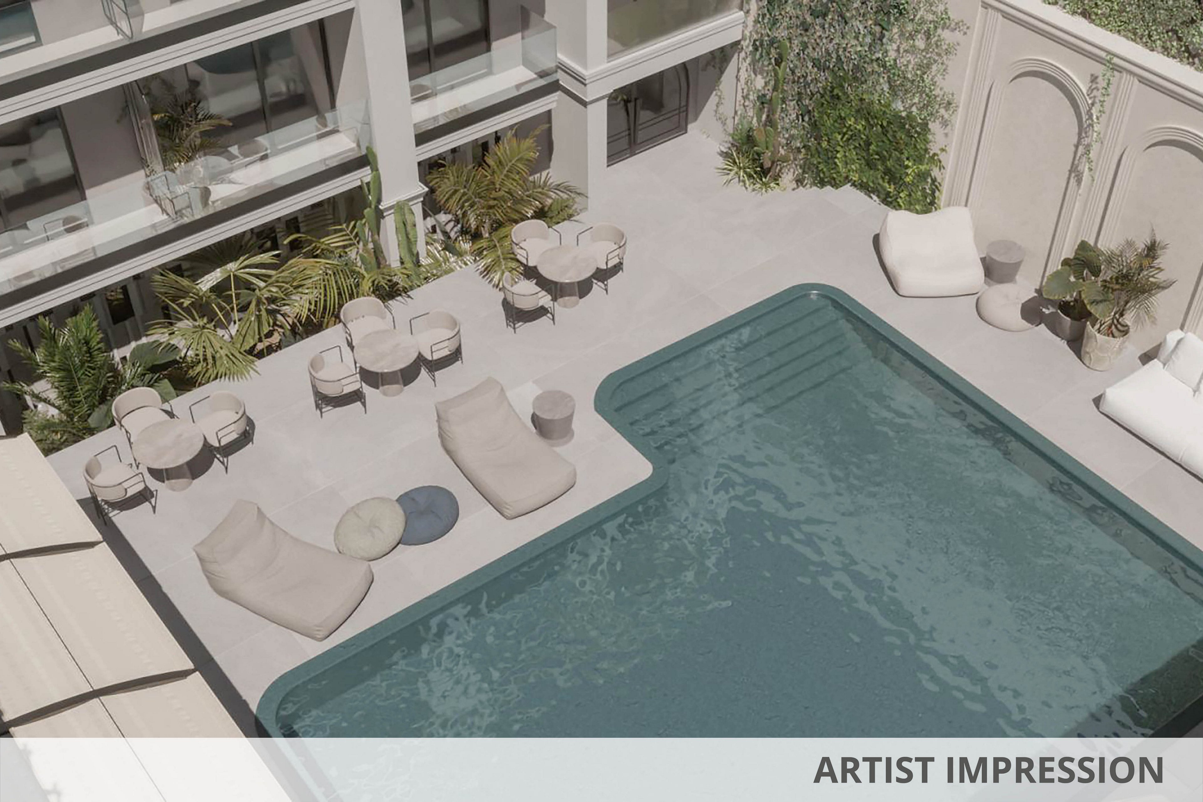 A contemporary hotel courtyard features a rectangular outdoor swimming pool surrounded by minimalist lounge chairs and tables. The setting is bright and tranquil, with neutral tones and lush greenery adding to the relaxing atmosphere. No people are present, emphasizing the serene and inviting environment. The architectural details include arched walls and large windows overlooking the pool area.