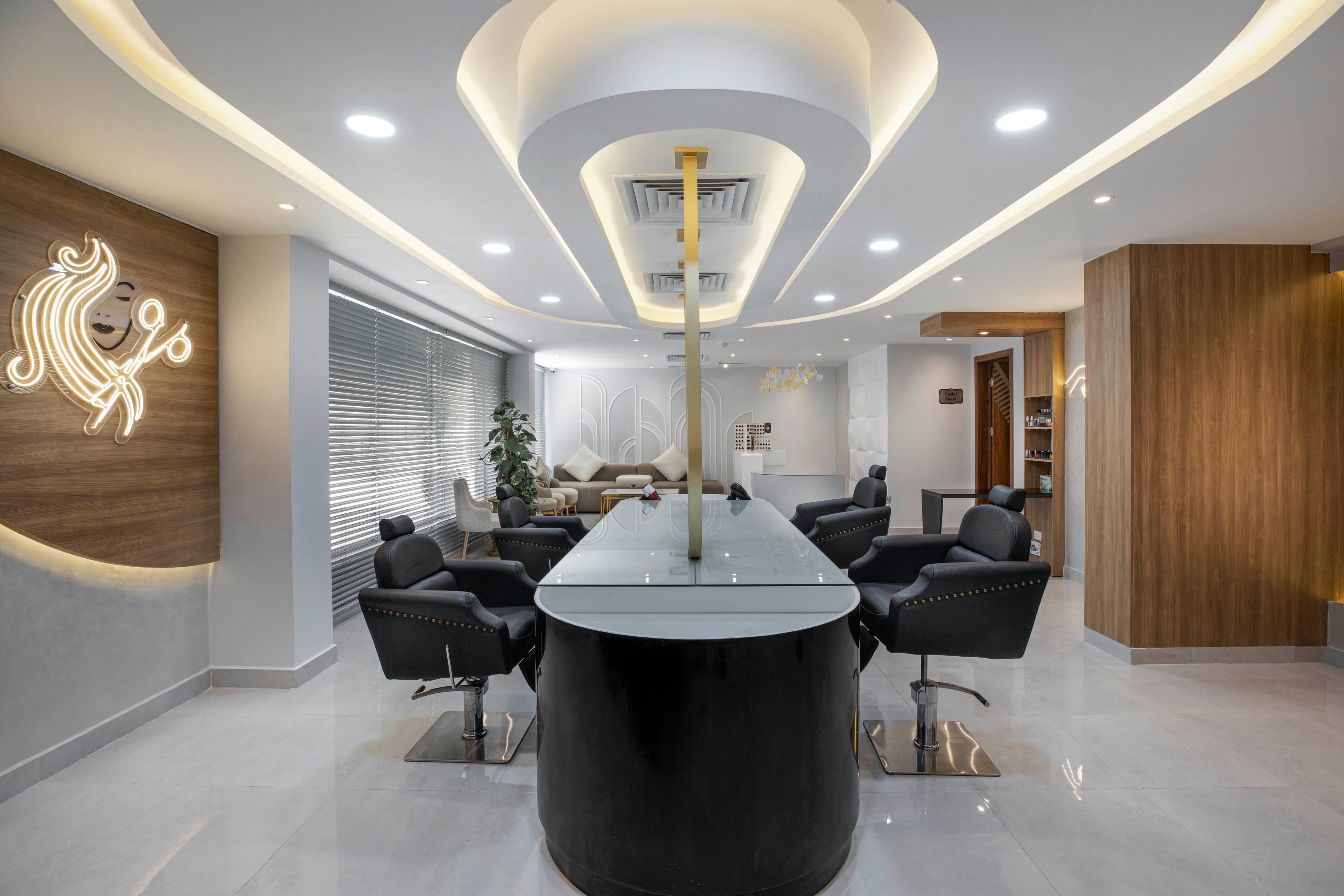 This image showcases a contemporary salon interior featuring sleek black chairs arranged around a central workstation. The setting is bright and spacious, with white walls, wood accents, and ambient ceiling lighting. A stylized illuminated lion graphic with the number '9%' is visible on a wooden panel. The overall mood is professional and inviting, with a neutral color palette and modern design elements.
