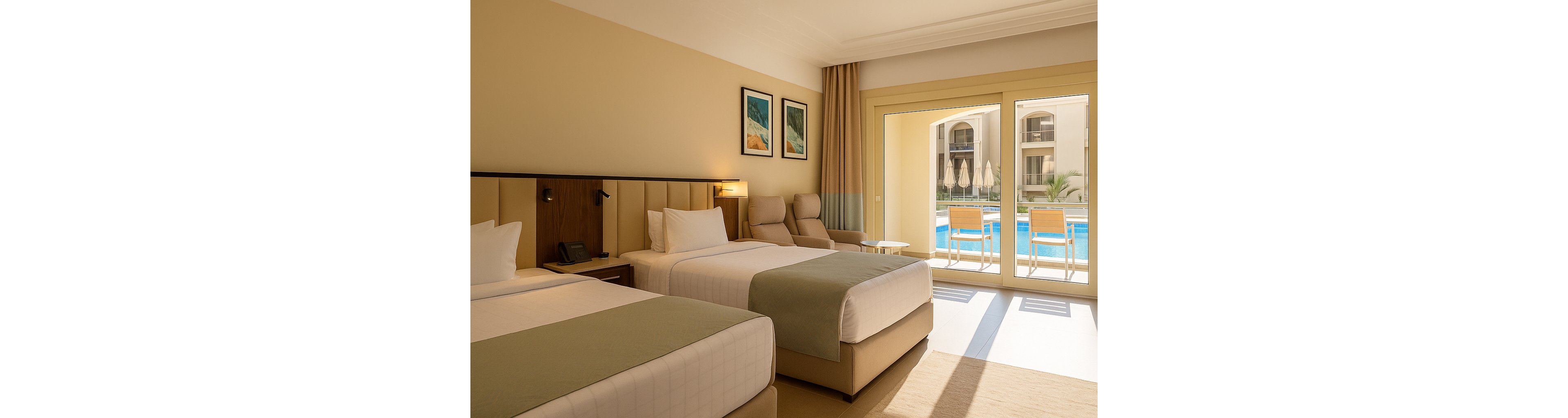 A spacious hotel room features two neatly made twin beds with light bedding and a contemporary headboard. The room is decorated in neutral tones with minimalistic artwork on the wall and a comfortable armchair near the window. Large glass doors open to a private patio with chairs, overlooking a sunlit swimming pool and resort buildings. The setting is bright and inviting, ideal for relaxation or vacation stays.