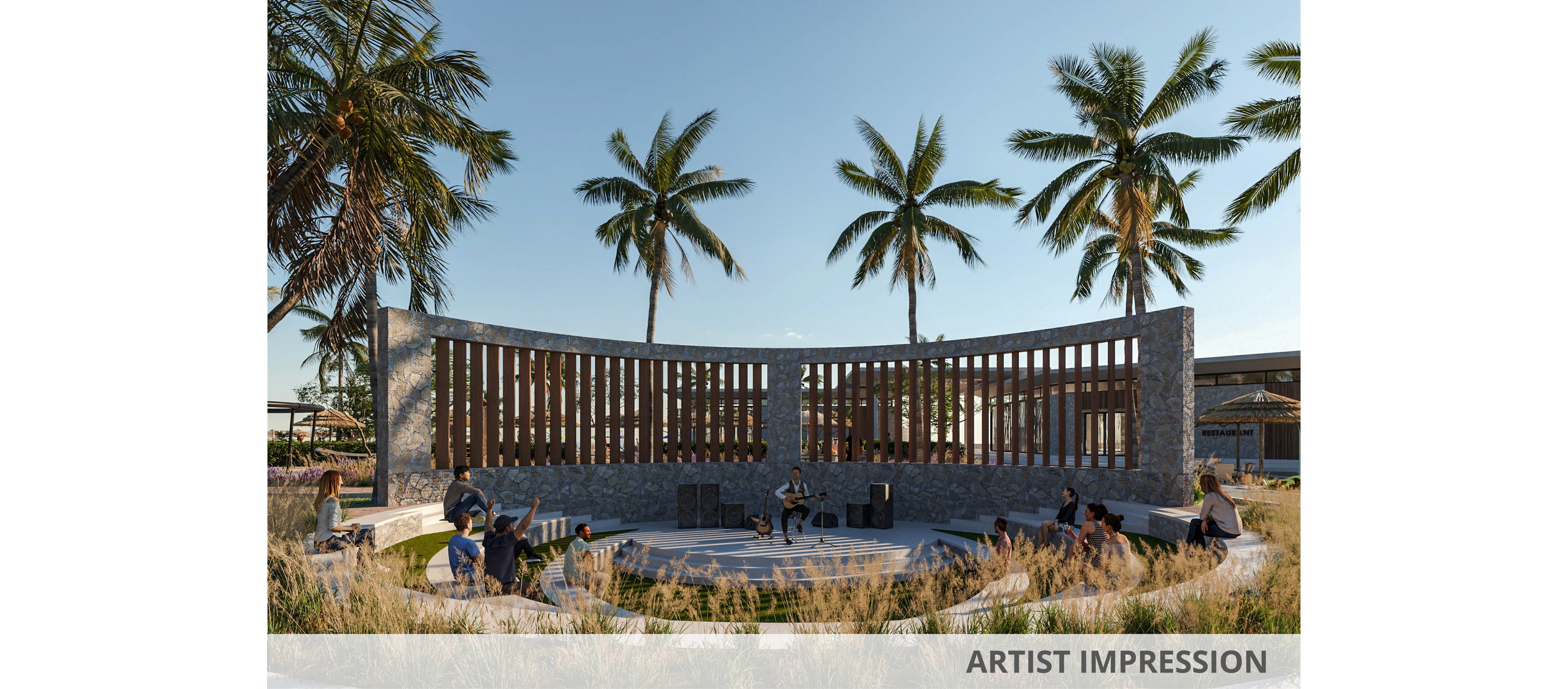 An open-air amphitheater is surrounded by tall palm trees and ornamental grasses under a clear sky. People sit and stand around the circular seating area, suggesting a casual gathering or performance. The curved stone wall with vertical wooden slats forms a striking architectural backdrop. Warm, low-angle sunlight creates long shadows and a relaxed, tropical atmosphere.