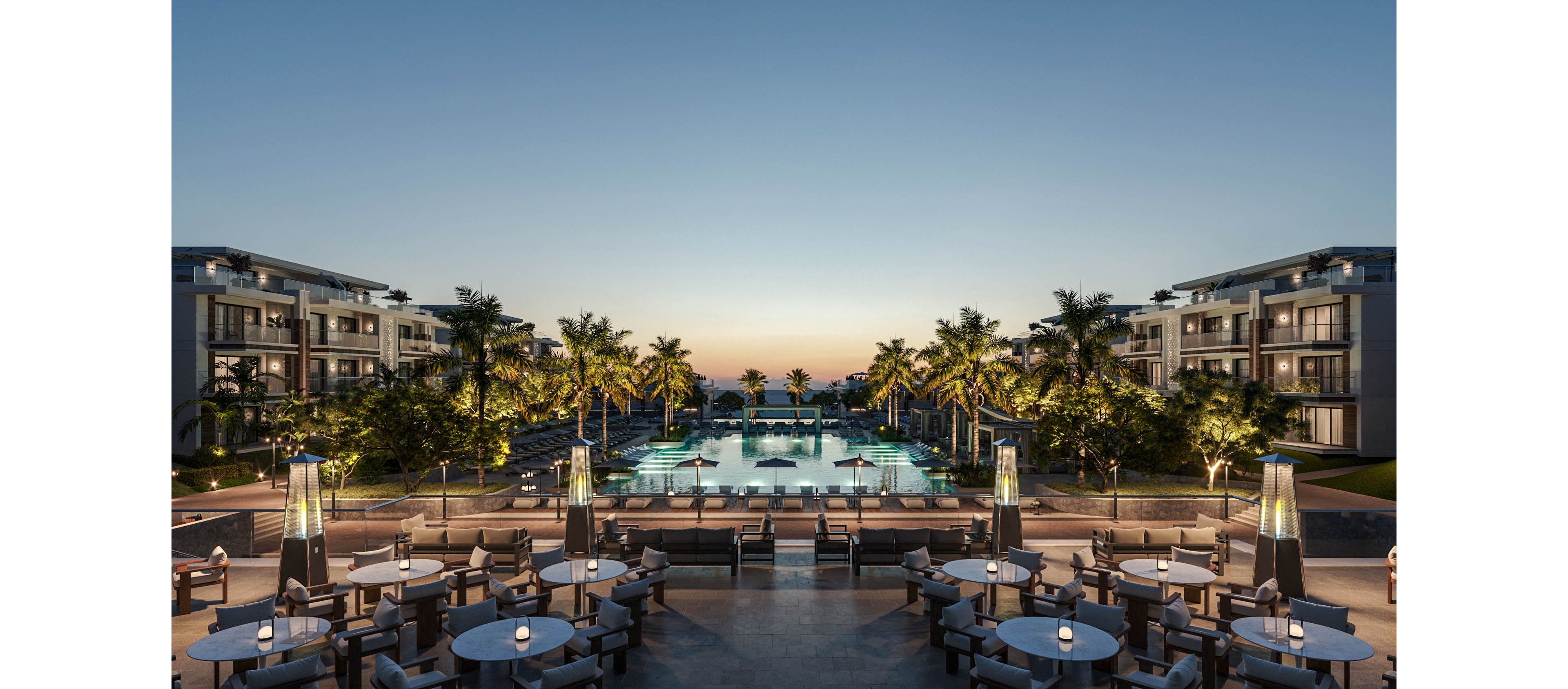 A luxurious resort features an expansive central swimming pool framed by palm trees at dusk. Elegant outdoor dining tables with glowing lights are arranged in the foreground, facing the illuminated pool. Modern low-rise hotel buildings line both sides, leading the eye toward the ocean horizon and colorful evening sky. The overall scene conveys an upscale, tranquil vacation atmosphere with refined outdoor amenities.