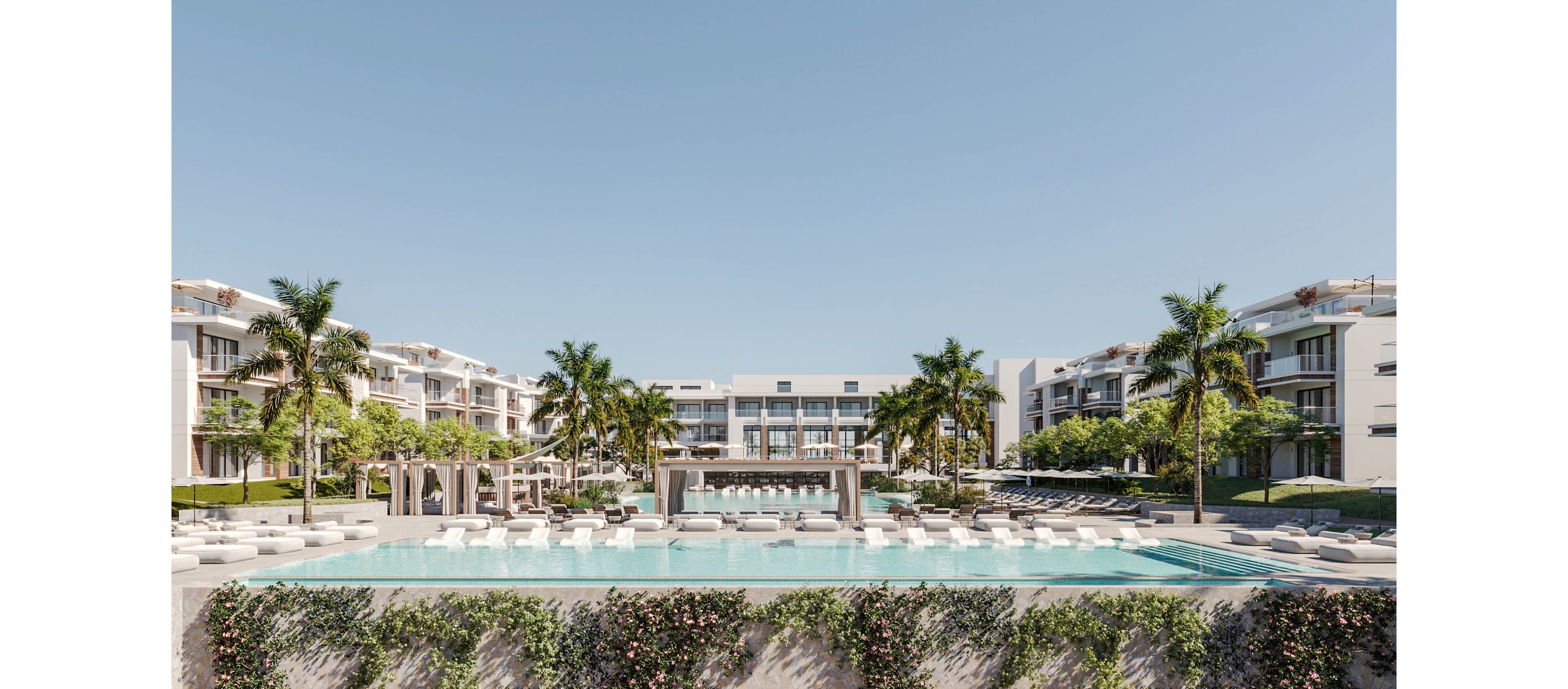 A contemporary resort complex features a large infinity pool as the central focal point. White lounge chairs and cabanas line the poolside, creating a luxurious and relaxing atmosphere. Palm trees and manicured greenery frame the scene, with multi-story hotel buildings in the background. The clear blue sky and calm water emphasize a warm, sunny vacation setting.