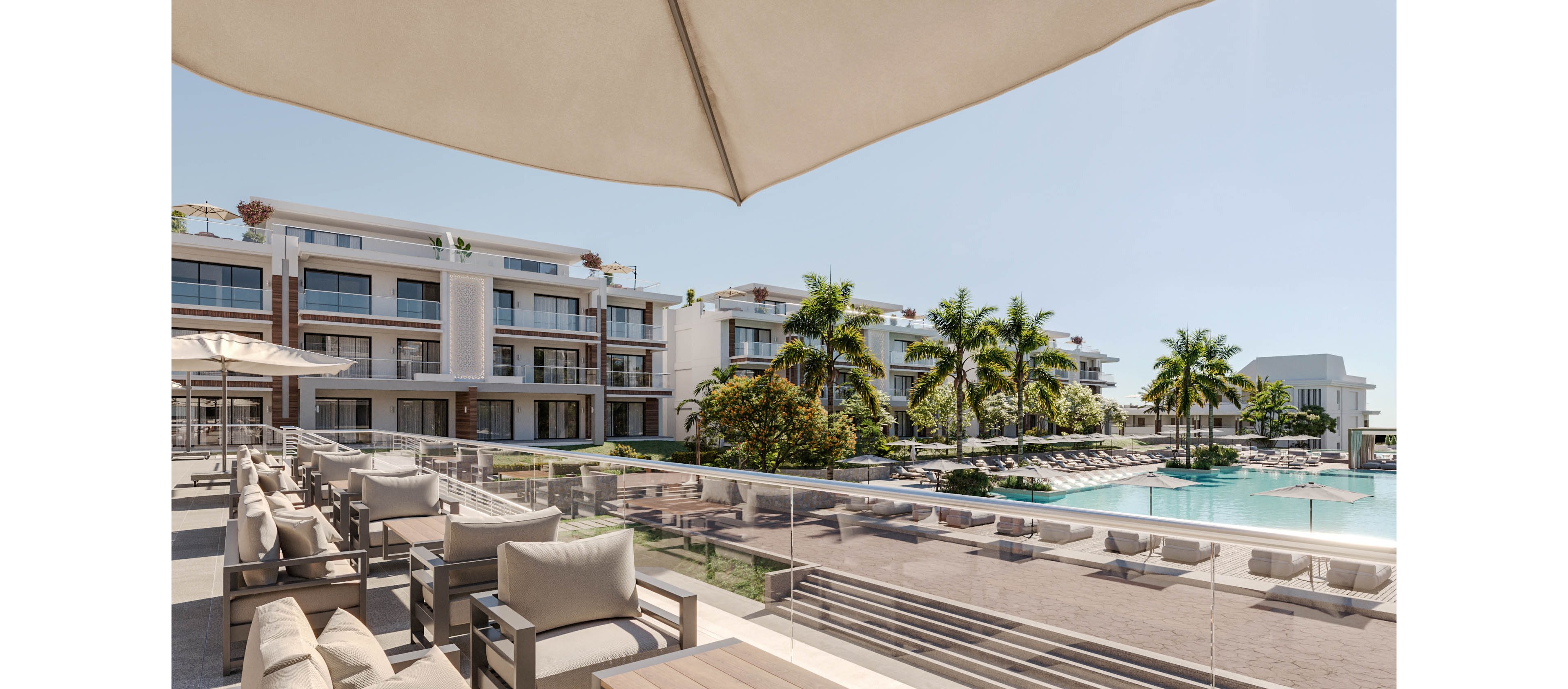 A modern luxury resort features a spacious poolside terrace with cushioned lounge seating. Contemporary multi-story buildings with balconies overlook the large swimming pool. Palm trees and manicured landscaping create a tropical atmosphere under a clear blue sky. Sun loungers and umbrellas surround the pool, suggesting a relaxing vacation setting. The scene feels calm, bright, and inviting for outdoor leisure.