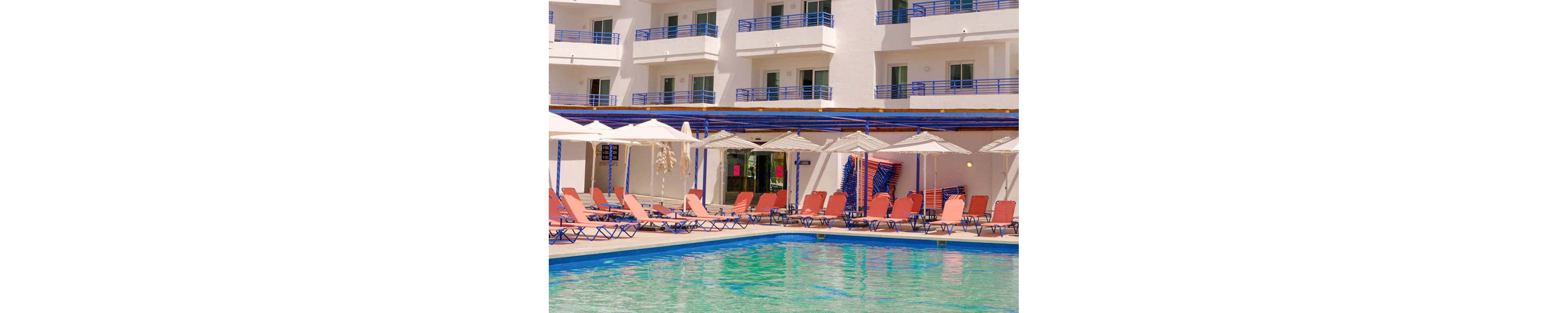 A clear turquoise swimming pool sits in front of a modern multi-story resort hotel. Rows of orange sun loungers and white umbrellas line the poolside, suggesting a relaxing vacation setting. The building features white walls with blue balcony railings under a bright blue sky. The overall scene conveys a warm, sunny, and inviting holiday atmosphere.