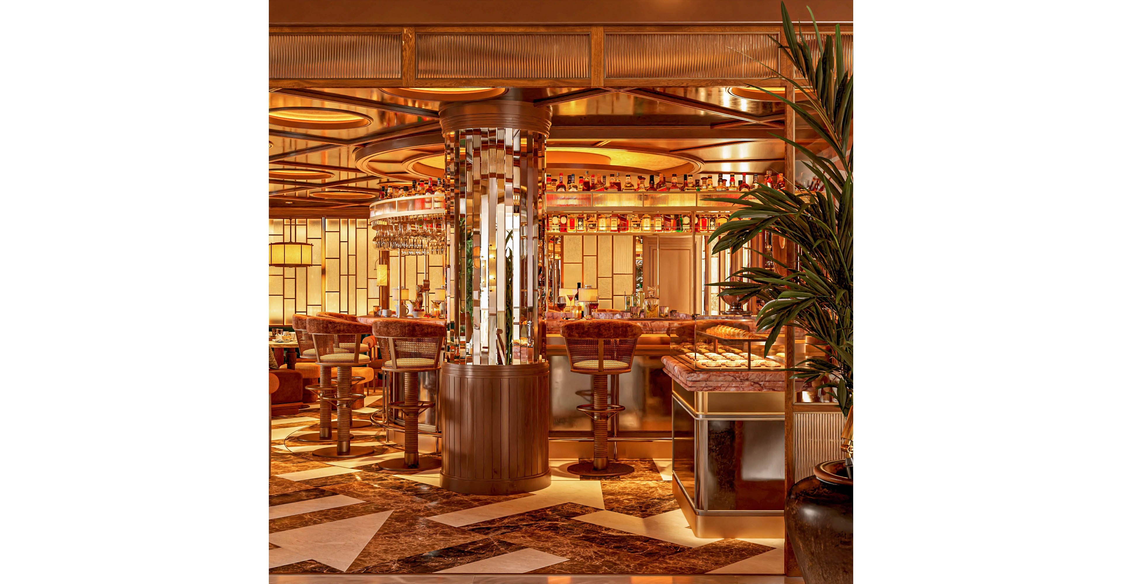 Opulent bar interior featuring a circular counter surrounded by high stools and a central mirrored column. Warm golden lighting reflects off metallic surfaces, glassware, and bottles arranged along the back bar. Geometric floor patterns and art deco-inspired details create a sophisticated, upscale atmosphere. Lush indoor plants soften the scene, adding contrast to the rich amber and bronze tones.