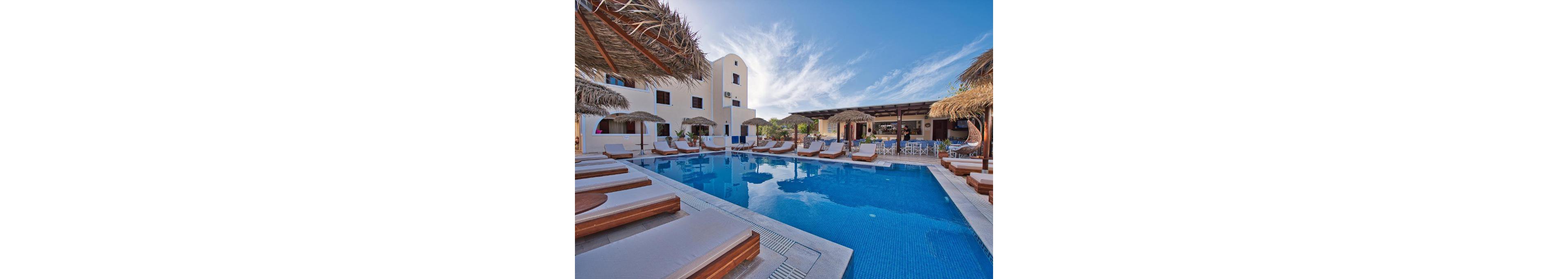 A serene outdoor pool surrounded by wooden lounge chairs and straw umbrellas at a luxury resort. The setting features a bright blue sky and Mediterranean-style architecture. The pool reflects the clear sky, creating a tranquil atmosphere for relaxation.
