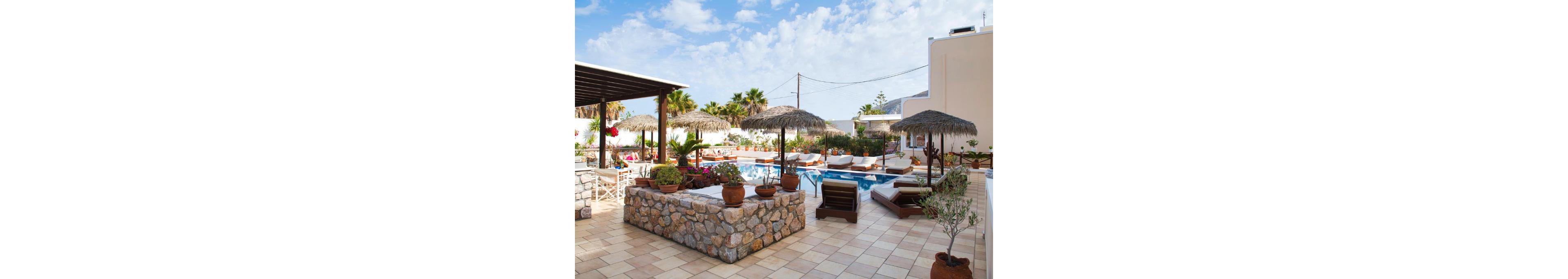 A serene outdoor pool area featuring straw umbrellas and lounge chairs surrounded by lush greenery and potted plants. The setting includes a tiled patio and a stone counter, creating a relaxing atmosphere. Bright blue skies and palm trees enhance the tropical vibe, perfect for leisure or vacation.