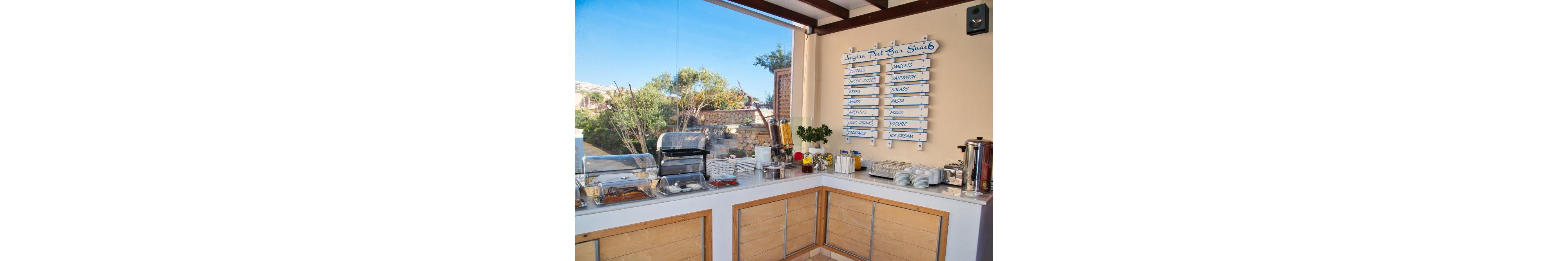 An outdoor snack bar setup featuring a menu board listing various food and drink options. The setting includes a counter with plates, cups, and food items, surrounded by greenery and natural light. Visible text on the menu includes items like 'Sandwiches', 'Juices', and 'Ice Cream'. The environment suggests a casual and relaxed dining atmosphere.