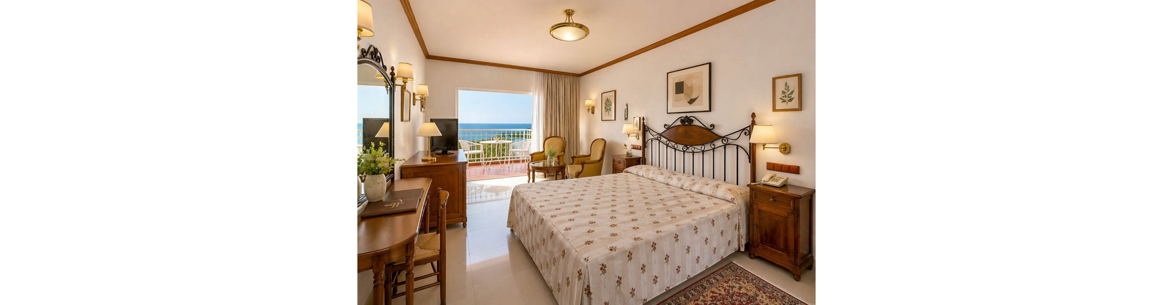 A neatly made double bed with a patterned bedspread is the focal point of this cozy hotel room. Classic wooden furniture, including a desk, chairs, and bedside tables, creates a warm and traditional atmosphere. Framed artwork and wall lamps add decorative touches, while a large open doorway leads to a balcony with a clear view of the sea and blue sky. Soft natural light fills the room, highlighting its inviting and comfortable design.