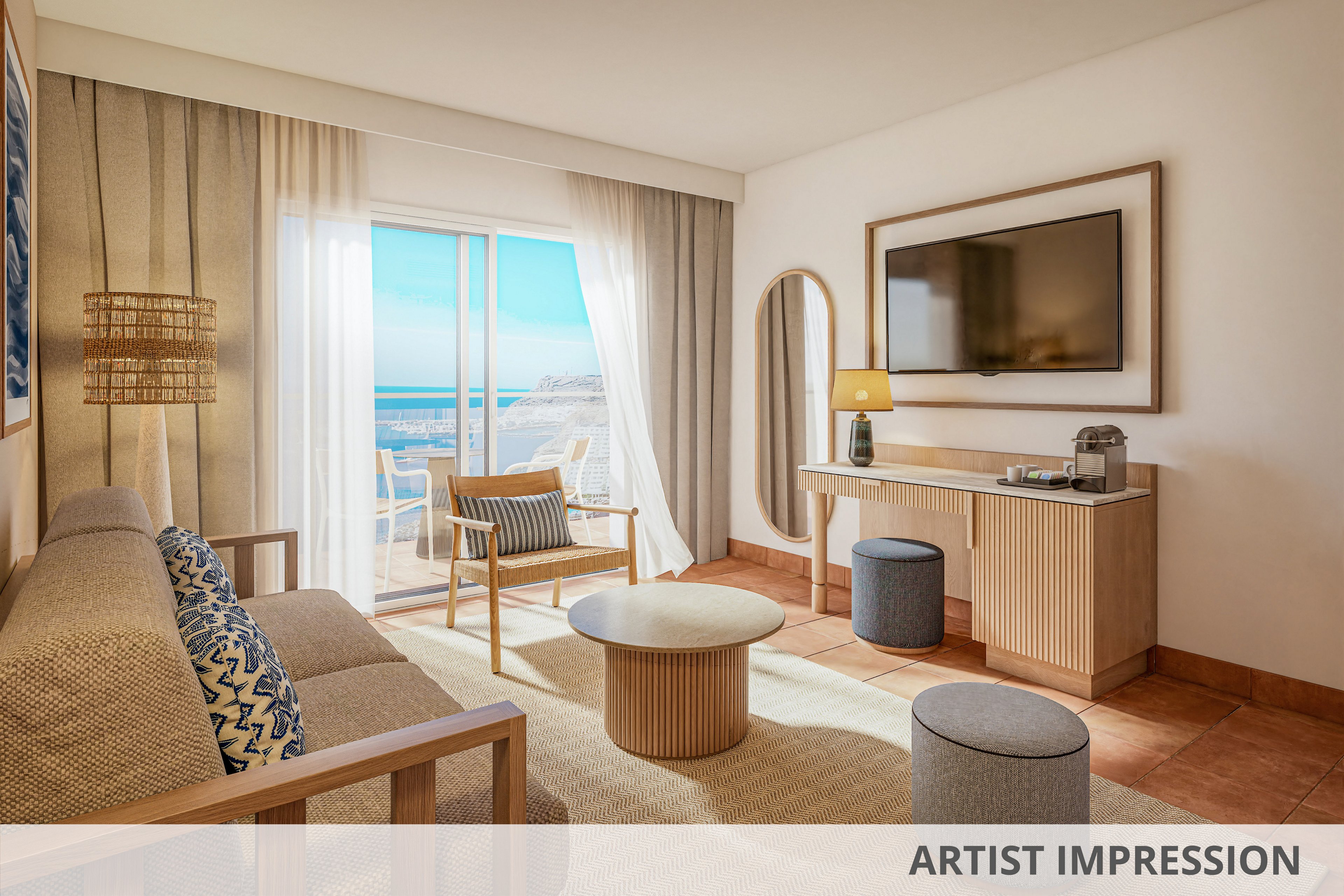 A modern hotel suite features a neutral-toned living area with a sofa, round coffee table, and wall-mounted television. Large glass doors open to a balcony overlooking a bright blue ocean and coastline. Light wood furniture, woven textures, and soft beige fabrics create a warm, relaxed atmosphere. Natural sunlight fills the room through sheer curtains, highlighting the contemporary coastal design.