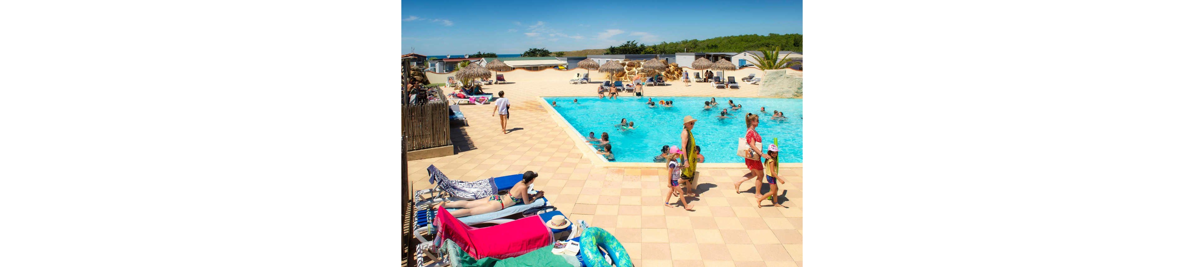 Families and children relax and play in a bright blue outdoor swimming pool at a holiday resort. People lounge on sunbeds under the clear sky while others swim and wade in the water. Thatched umbrellas, beach huts, and palm trees create a tropical vacation atmosphere. The scene feels warm, casual, and family-friendly with vibrant summer colors.