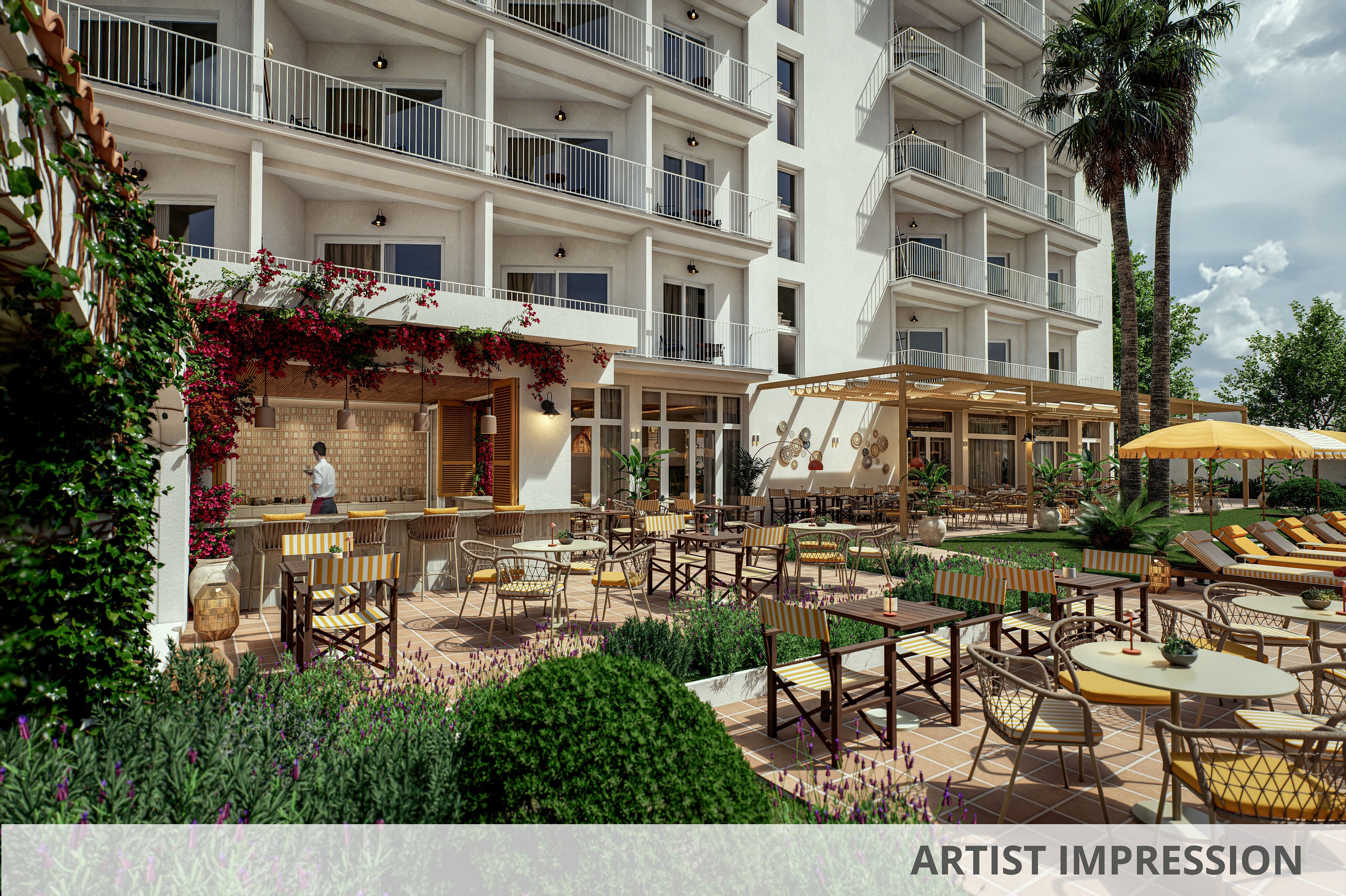 A hotel courtyard features an inviting outdoor bar and seating area surrounded by lush greenery. Numerous tables and chairs are arranged on a tiled terrace, with sun loungers and umbrellas positioned nearby for relaxation. A bartender stands behind the bar, while balconies from the multi-story hotel overlook the courtyard. Palm trees, flowering vines, and warm sunlight create a relaxed, Mediterranean-style atmosphere.