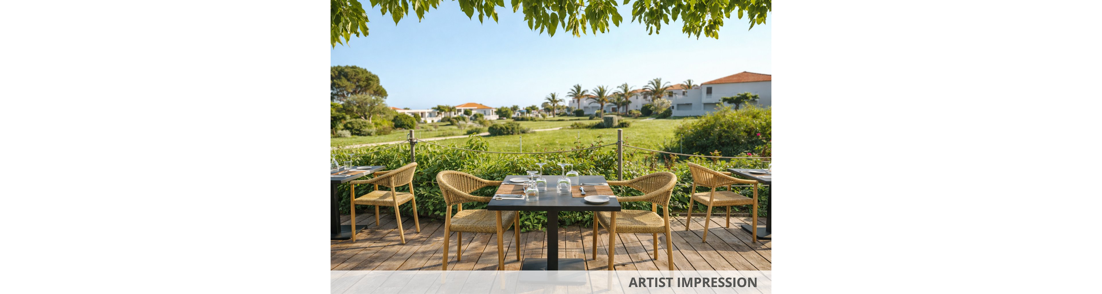 A sunlit outdoor restaurant terrace features neatly set tables and wicker chairs, facing a lush green lawn. The setting is tranquil, with modern white villas and palm trees visible in the background under a clear blue sky. The wooden deck and leafy overhead branches add a natural, relaxed ambiance. No people are present, emphasizing the peaceful atmosphere. Table settings include glassware, plates, and cutlery, ready for guests.