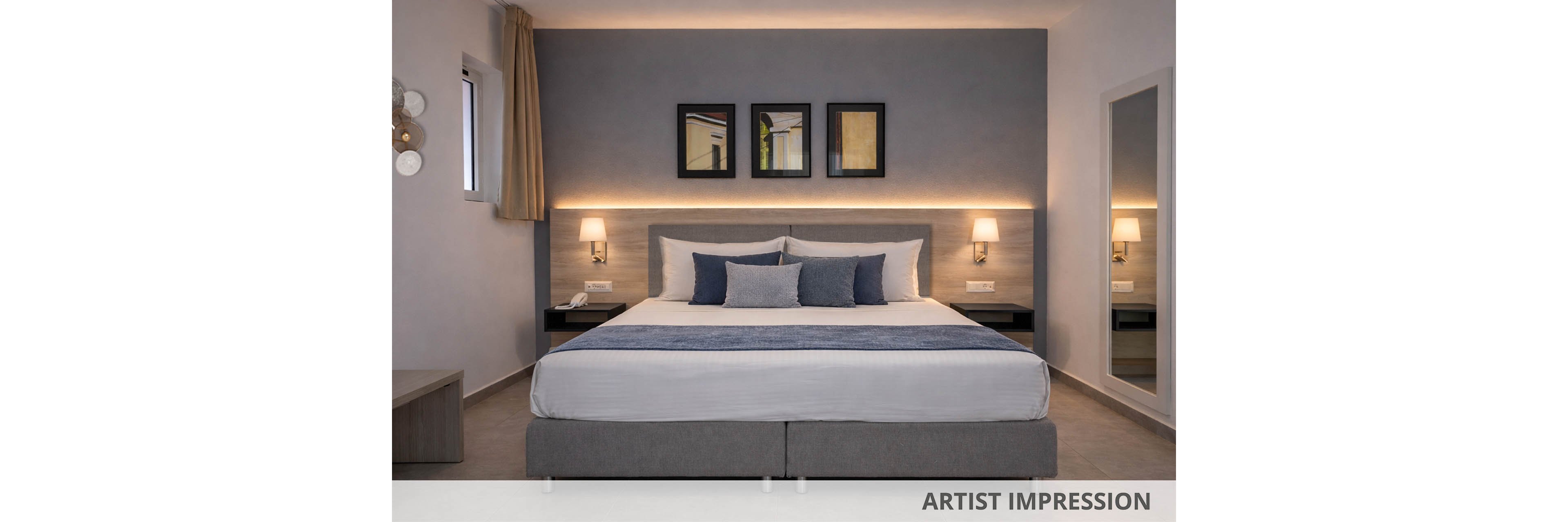 A contemporary hotel room features a large double bed with gray and blue bedding, flanked by two wall-mounted lamps. The setting is minimalistic, with a neutral color palette and soft lighting creating a calm atmosphere. Three framed artworks hang above the bed, and a large mirror is visible on the right wall. The room is tidy and uncluttered, emphasizing comfort and modern style.