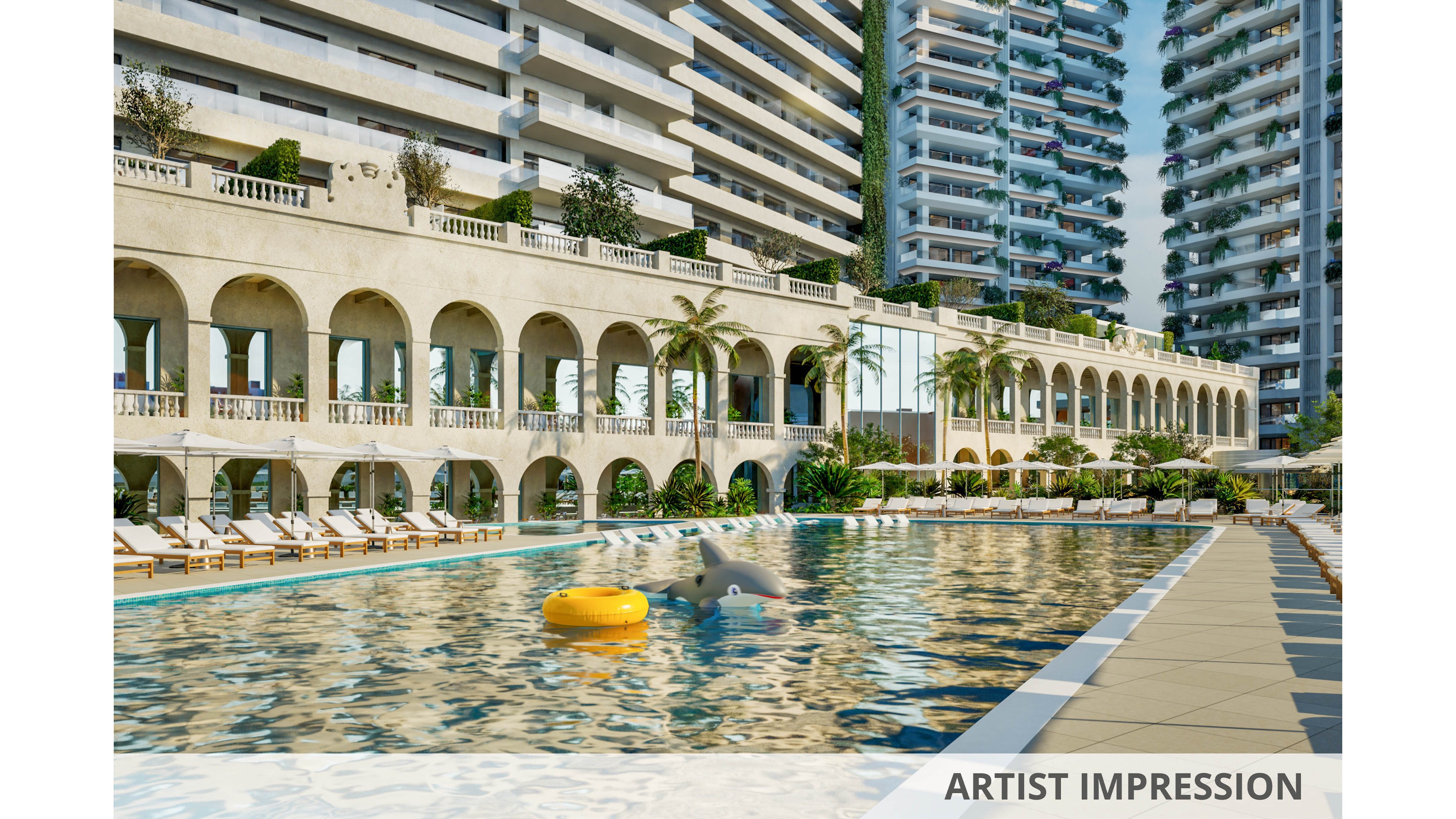 A large outdoor swimming pool is set in front of a grand hotel or residential building with arched architecture. The pool features a yellow inflatable ring and a dolphin float, surrounded by numerous white loungers and umbrellas. Tall modern buildings and palm trees create a resort-like atmosphere, with clear reflections on the water. The setting is bright and inviting, suggesting a relaxing vacation mood.