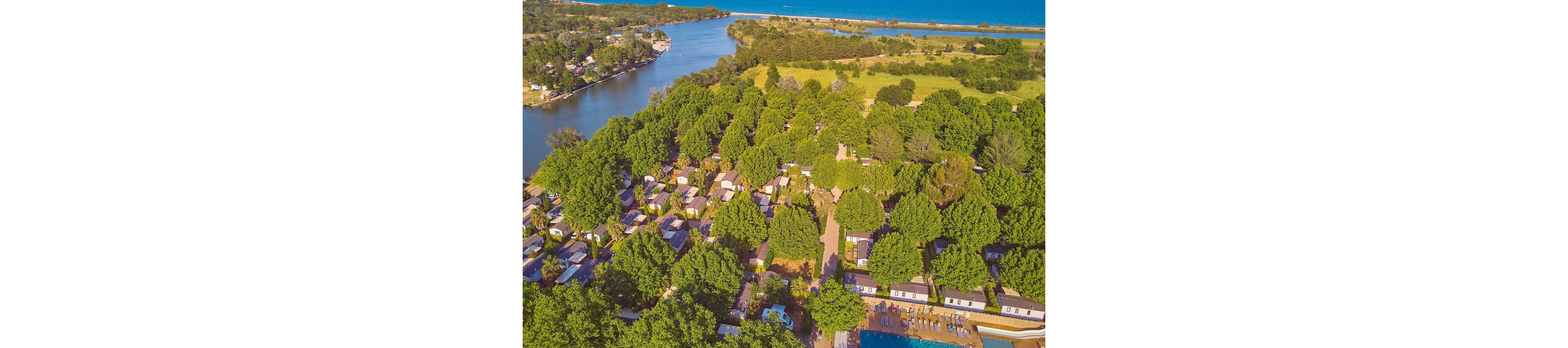An aerial perspective showcasing a serene lakeside vacation area with numerous cabins surrounded by lush green trees. The setting includes a swimming pool and a winding river leading to a large lake. The vibrant natural scenery highlights relaxation and outdoor leisure activities.