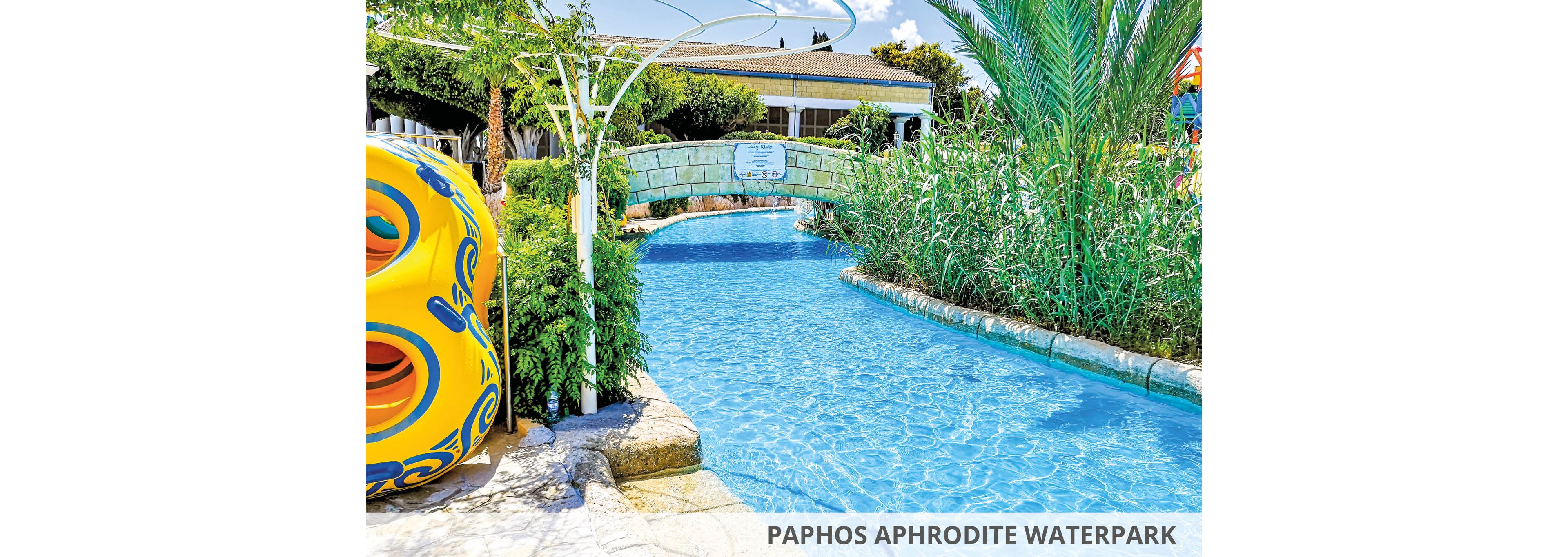 A vibrant waterpark featuring a serene lazy river surrounded by lush greenery and colorful structures. The setting includes a stone bridge and tropical plants, creating a relaxing atmosphere. The text 'Paphos Aphrodite Waterpark' is clearly visible in the image.
