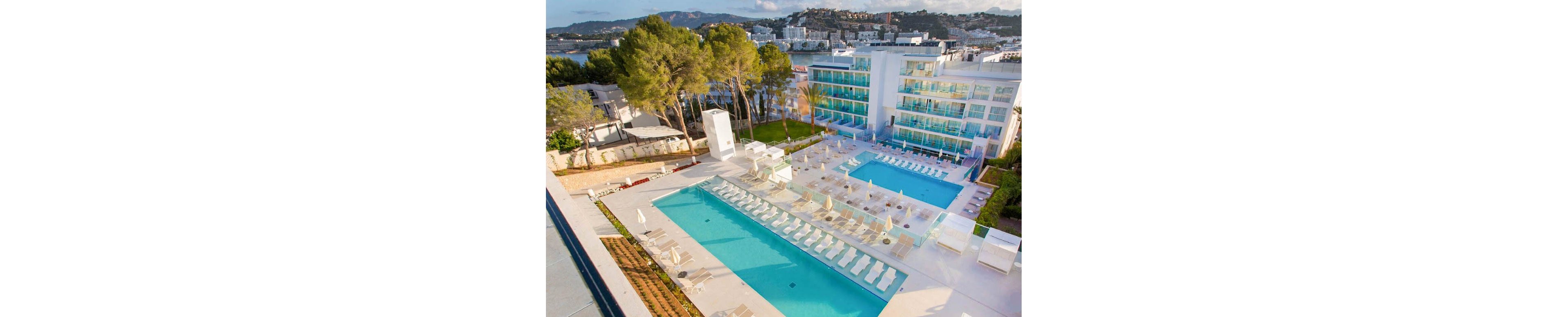 The image shows a contemporary hotel complex featuring two large outdoor swimming pools surrounded by sun loungers and umbrellas. The setting is a sunny, resort-style environment with lush trees and hills in the background. The mood is relaxed and inviting, with a clean, minimalist palette dominated by white and blue tones. No visible text or numeric values are present in the image.