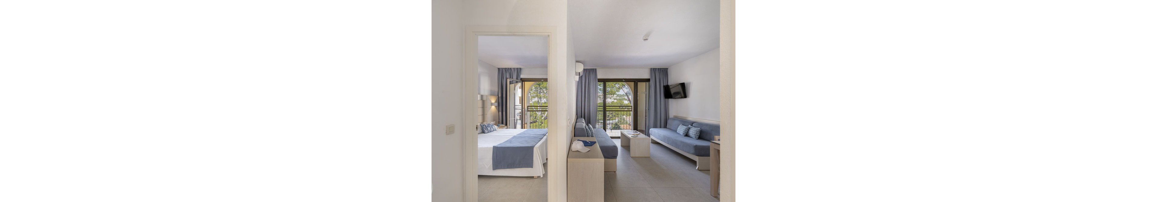 The image shows a contemporary hotel suite divided into a bedroom and a living room. Both spaces feature large windows with blue curtains, letting in natural light and offering views of greenery outside. The bedroom has a neatly made bed with blue and white linens, while the living area includes a sofa, coffee table, and wall-mounted TV. The overall palette is neutral with blue accents, creating a calm and inviting atmosphere.