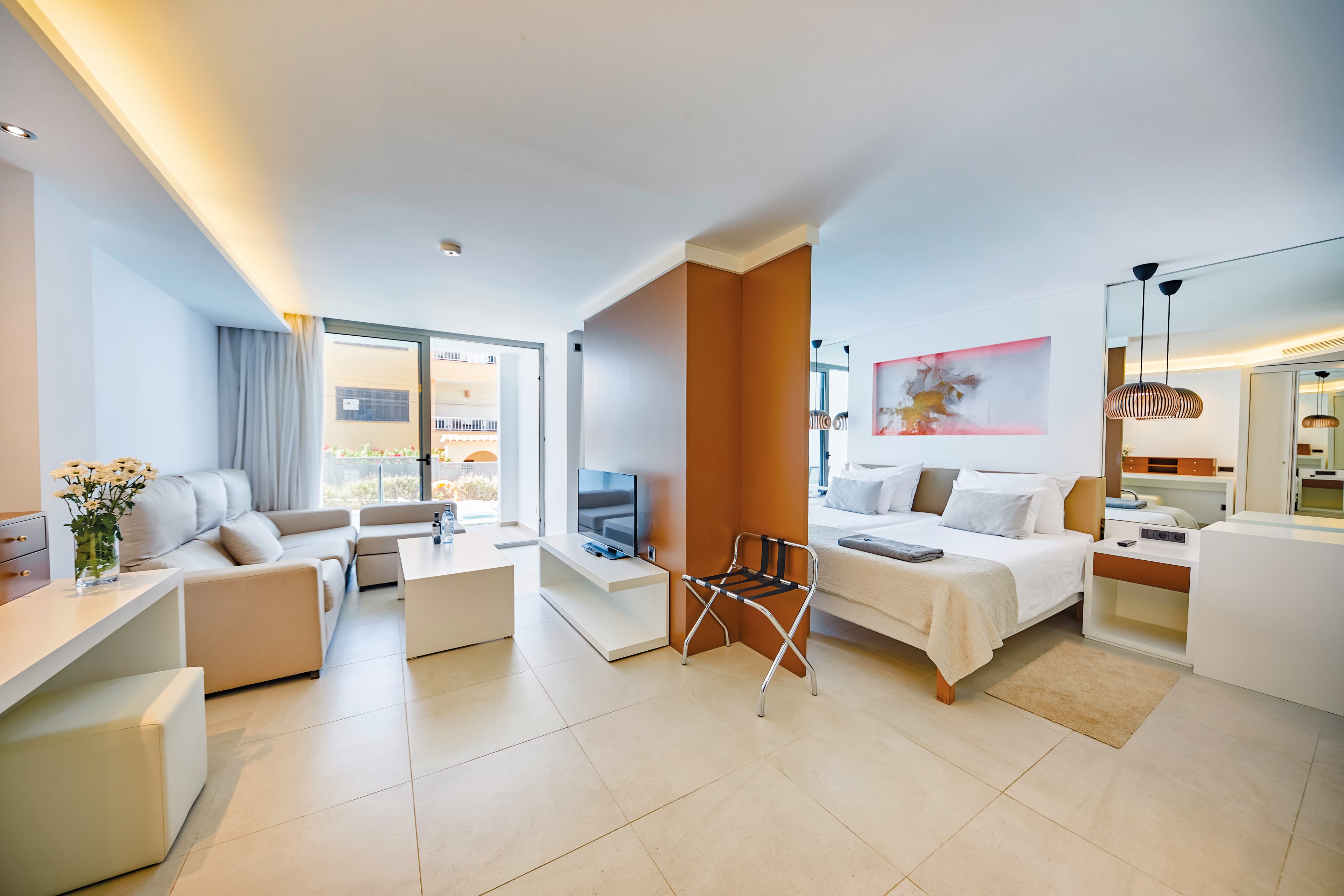 A contemporary studio apartment featuring an open layout with a living area, bedroom, and kitchenette. The setting includes bright natural light from large windows and a balcony view. Neutral tones dominate the palette, complemented by minimalist furniture and decor. The space is designed for comfort and functionality, ideal for urban living or vacation stays.