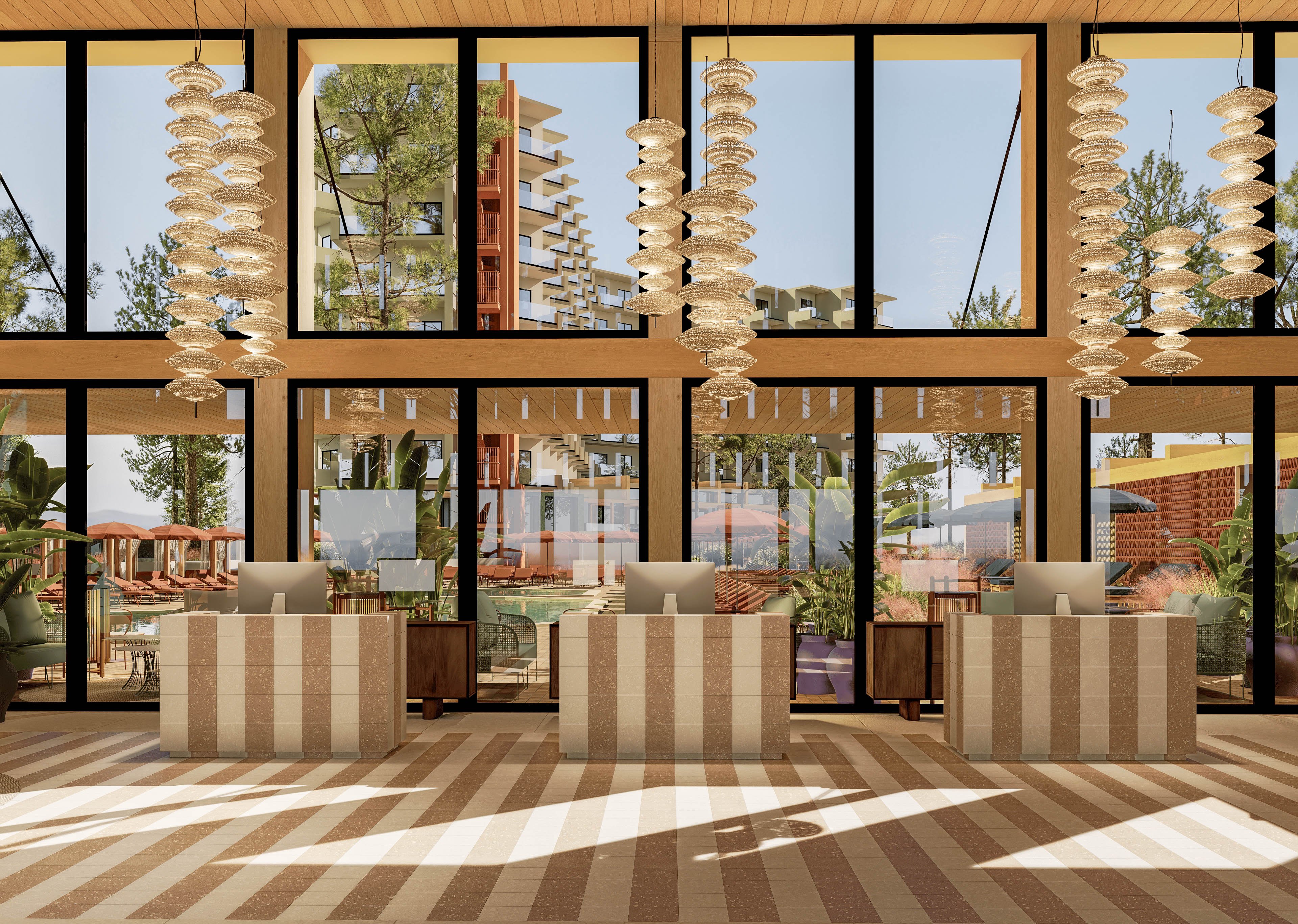 A contemporary reception area features three striped front desks, each equipped with a computer monitor. Large floor-to-ceiling windows reveal an outdoor resort setting with palm trees and multi-story buildings. Sculptural pendant lights hang from a wooden ceiling, adding visual interest and warmth. The striped flooring and neutral color palette create a stylish, inviting atmosphere suitable for a hotel or vacation property.