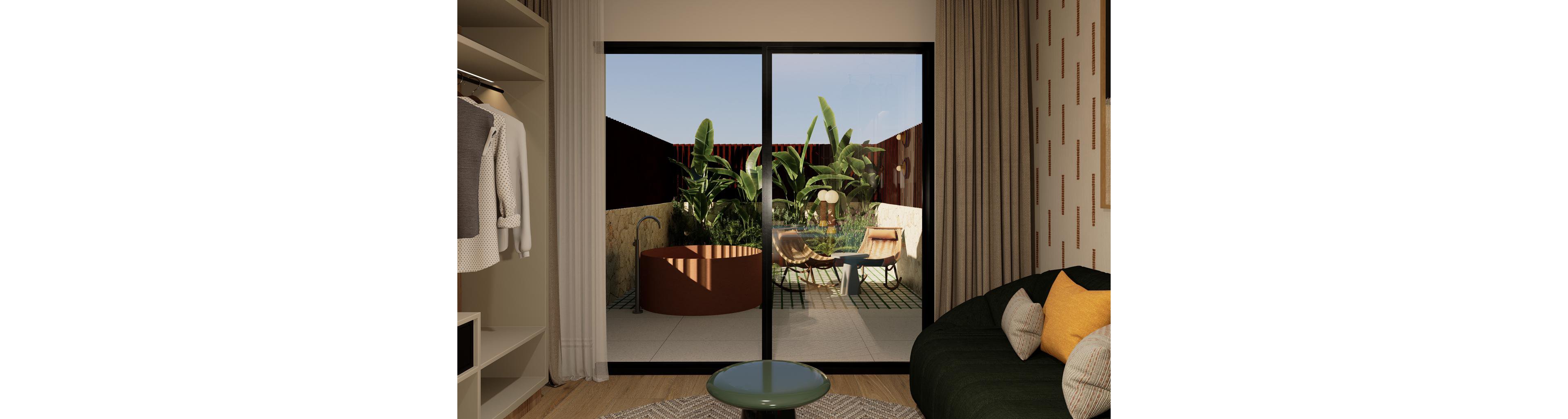 A contemporary bedroom interior opens onto a small tropical patio through large sliding glass doors. Inside, a dark green sofa with yellow and neutral cushions sits beside a round coffee table, with an open wardrobe visible on the left. Outside, a circular freestanding tub and a pair of lounge chairs with a small table create a cozy outdoor seating area surrounded by lush green plants. Warm neutral tones, soft lighting, and natural textures give the space a relaxed, modern resort feel.