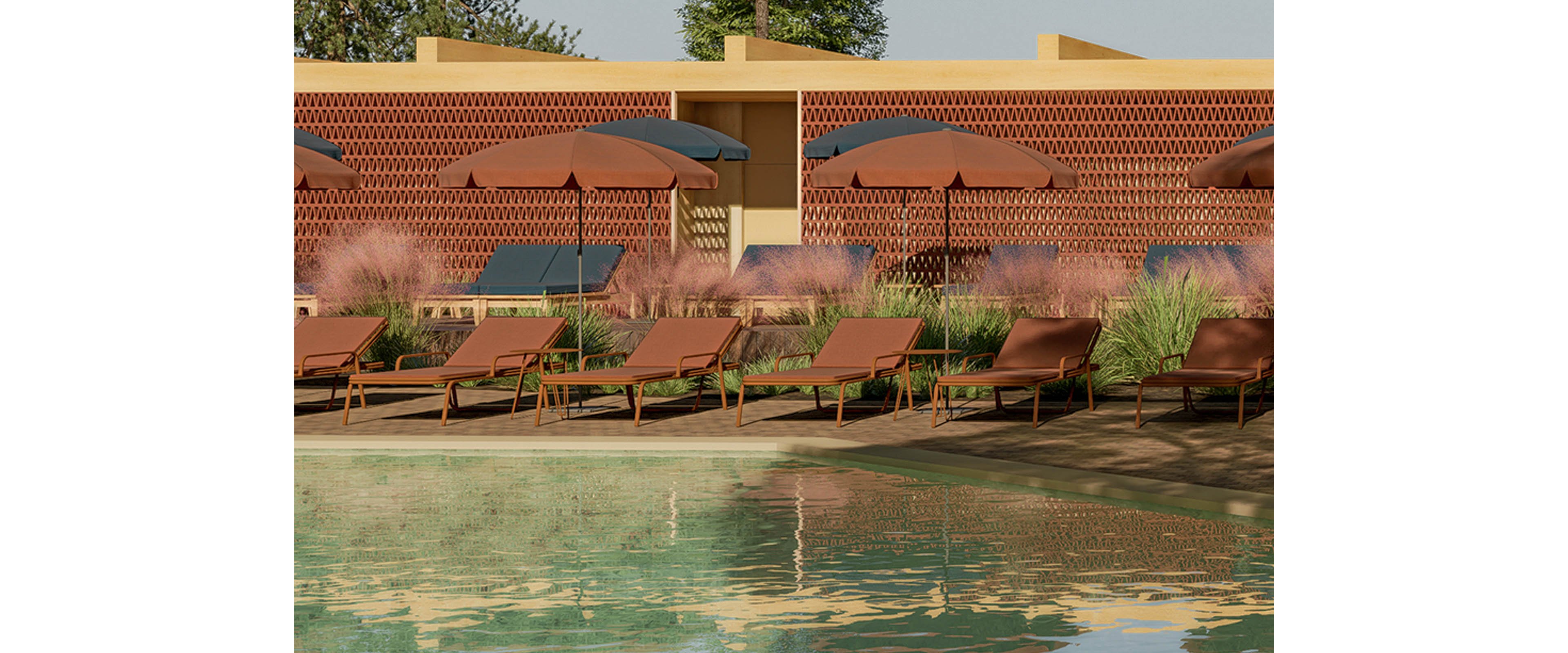 A row of contemporary lounge chairs and matching umbrellas lines the edge of a tranquil swimming pool. The setting appears to be an outdoor resort or modern hotel terrace with warm-toned architectural walls in the background. Tall ornamental grasses and plants soften the scene, adding texture and natural color. The overall atmosphere is calm and inviting, suggesting a relaxing leisure space for sunbathing and poolside rest.