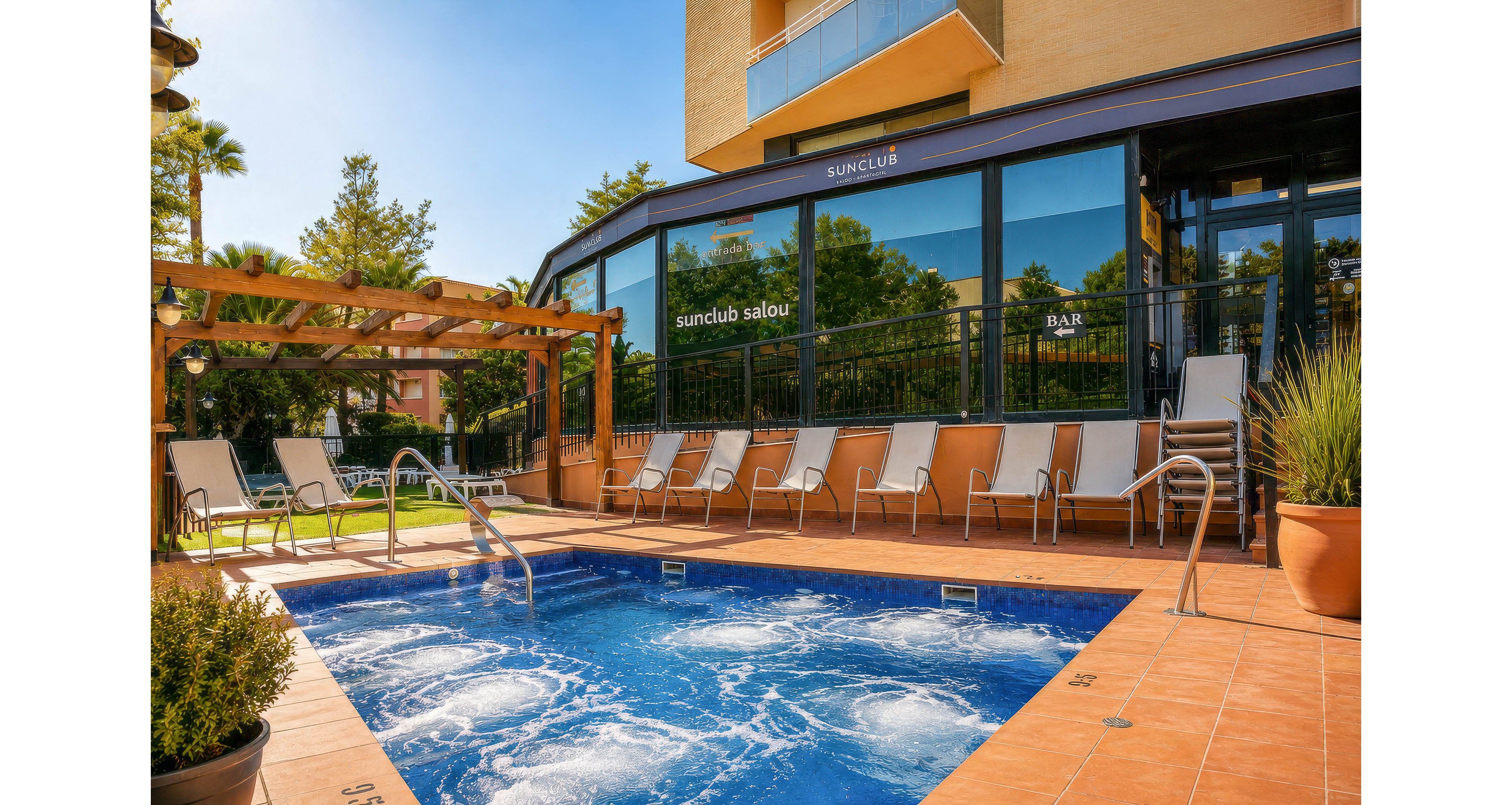 An outdoor jacuzzi pool bubbles on a tiled terrace beside a modern hotel building. Multiple reclining sun loungers line the edge of the pool and sit under a wooden pergola, suggesting a relaxing leisure setting. Glass walls reflect greenery and display the text "suncub salou" and "BAR" indicating a resort bar area nearby. Warm sunlight, orange tiles, and surrounding plants create a bright, inviting vacation atmosphere.