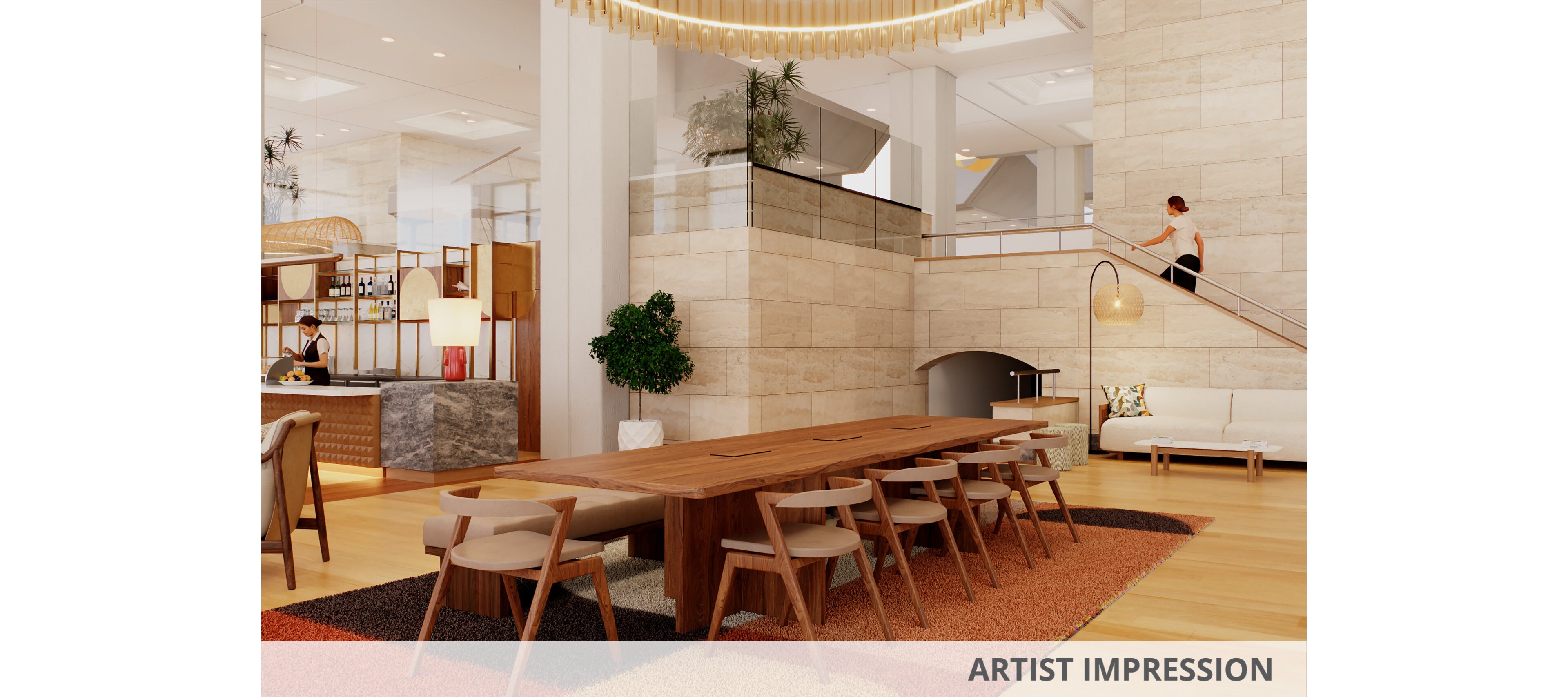 A spacious, contemporary hotel lobby features a long wooden communal table surrounded by chairs. Warm neutral stone walls and light wood flooring create an inviting atmosphere. A colorful patterned rug anchors the seating area, while a barista works behind a small bar in the background. A person walks down a staircase near a cozy lounge corner with a floor lamp and sofa.