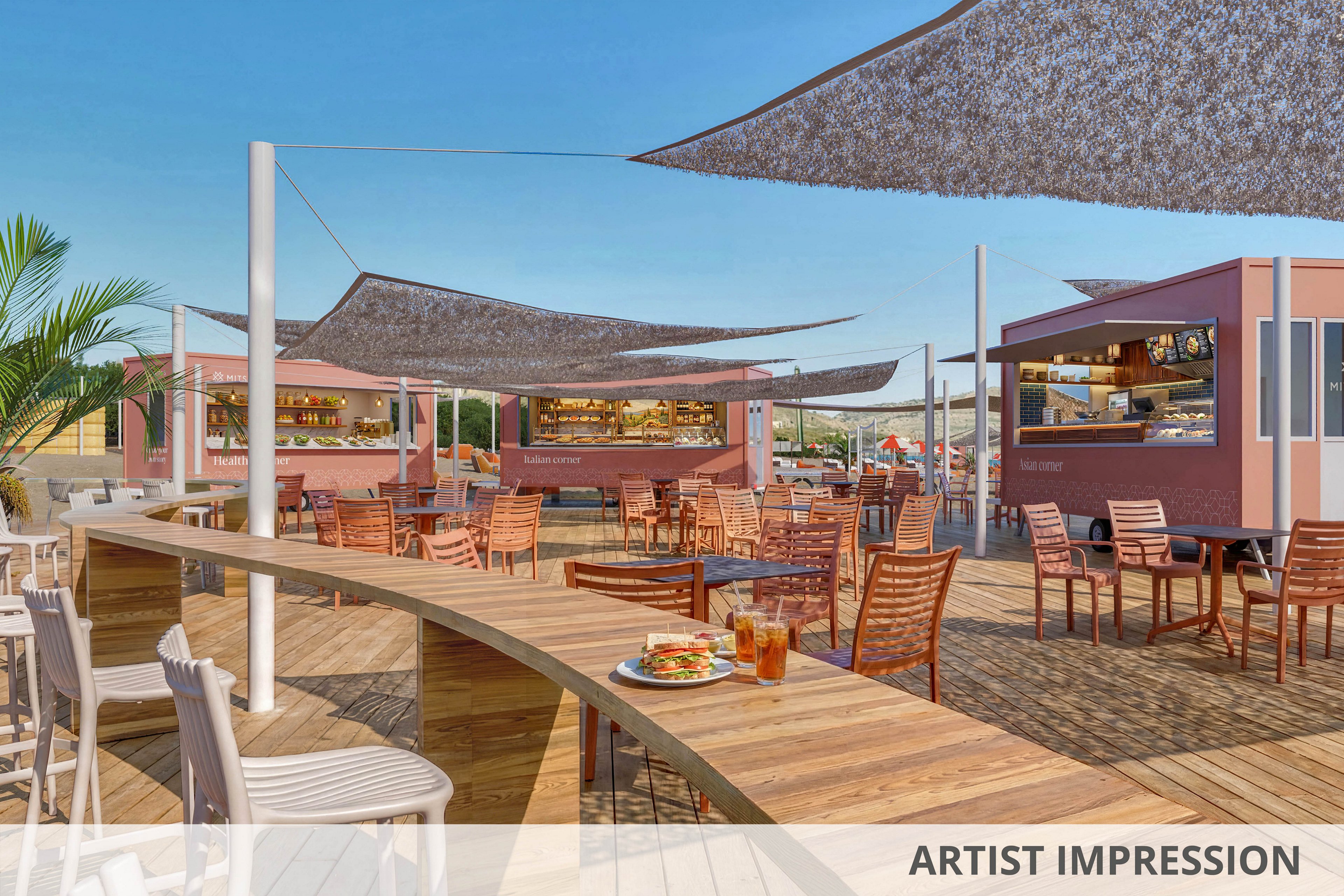An open-air dining area features wooden decking with several pink food trucks serving as bars and kitchens. Numerous wooden tables and chairs are arranged under large shade sails, creating a relaxed social space. In the foreground, a curved counter holds plates of food and iced drinks, inviting guests to sit and enjoy. A clear blue sky and a potted palm tree enhance the bright, summery atmosphere of the venue.