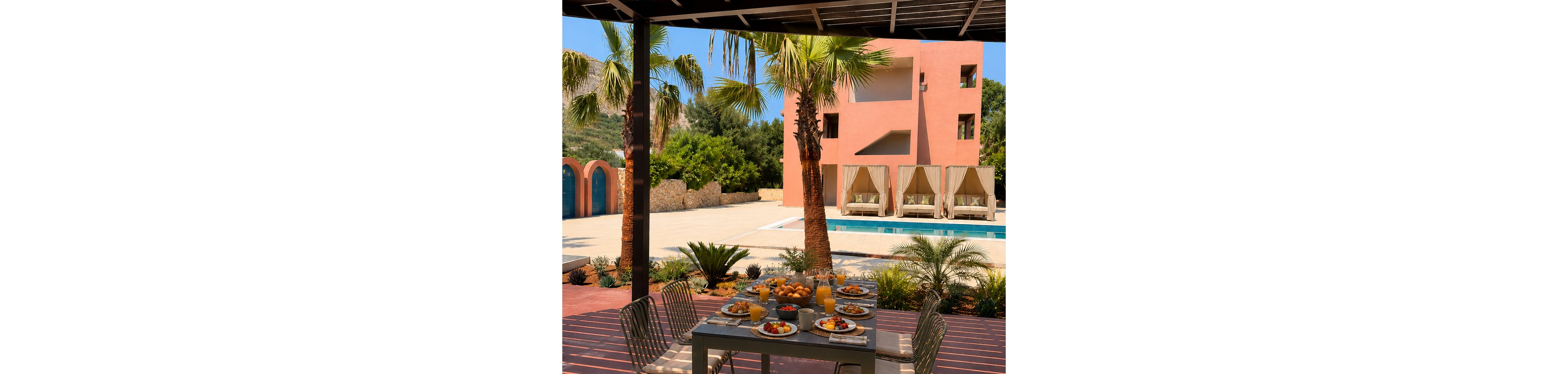 A table is set with a generous breakfast spread on a shaded terrace overlooking a swimming pool. Plates of fruit, pastries, and eggs are arranged alongside glasses of juice and coffee cups. Palm trees and lush greenery surround the pool area, creating a tropical resort atmosphere. In the background, a modern peach-colored building with cabana-style loungers suggests a relaxing vacation setting.