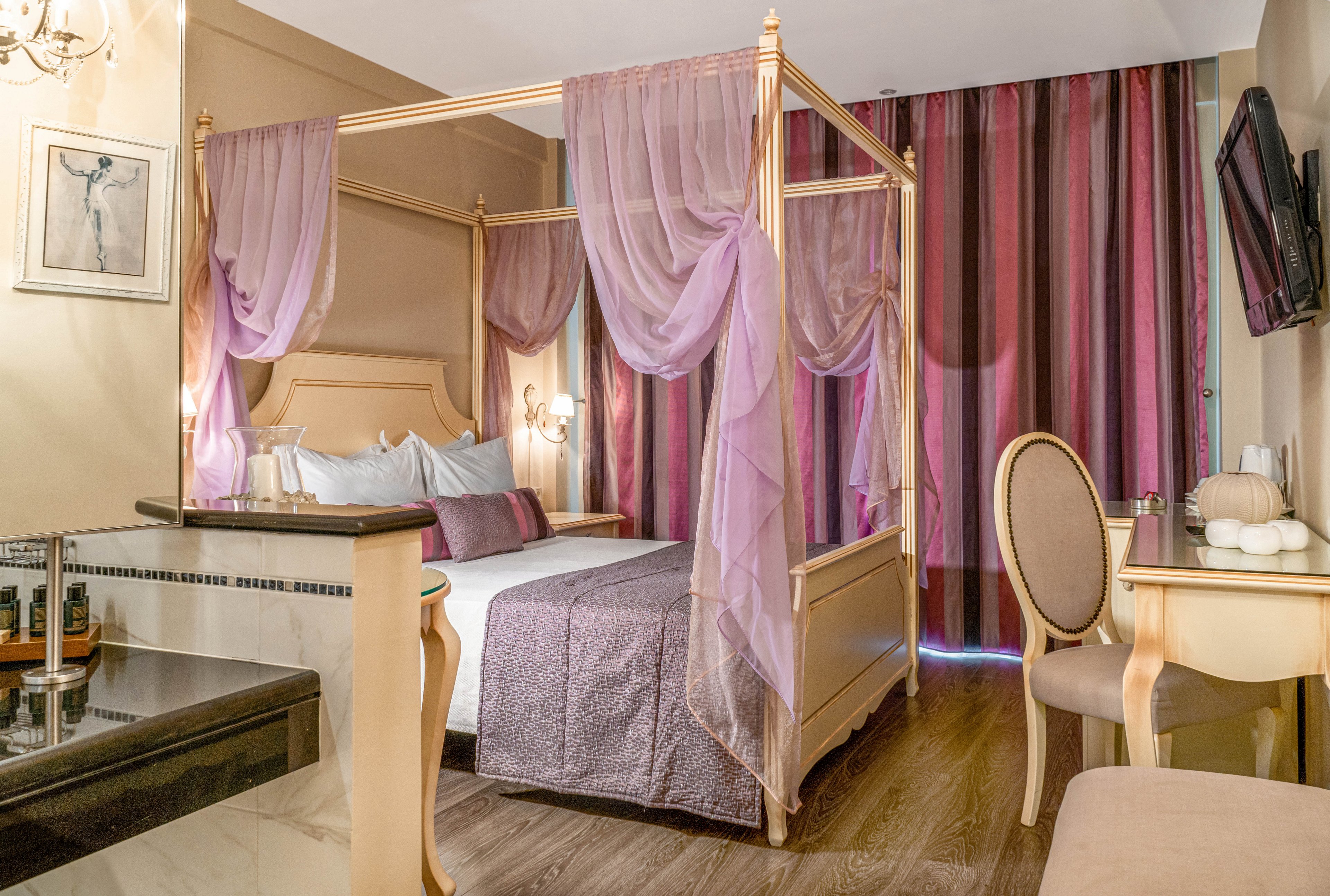 The main subject is a luxurious hotel suite featuring a four-poster bed adorned with sheer purple drapes. The room includes a desk, chair, and wall-mounted television, with striped purple curtains covering the window. Soft lighting and pastel tones create a cozy, romantic atmosphere. Decorative elements such as framed artwork and plush pillows enhance the stylish interior.