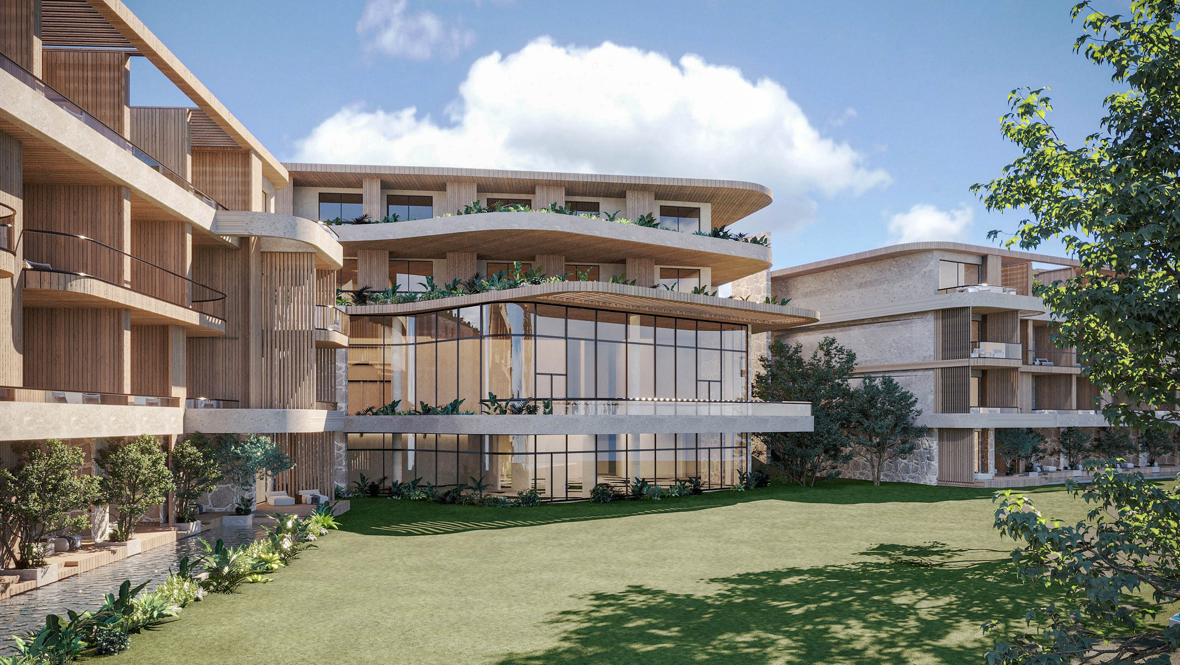 Contemporary multi-story residential buildings surround a central green lawn under a bright blue sky. The architecture features large glass windows, spacious balconies, and natural wood and stone finishes. Lush plants and landscaped greenery line the ground level and upper terraces, creating a resort-like atmosphere. Soft daylight and clear weather highlight the clean, modern design of the complex.