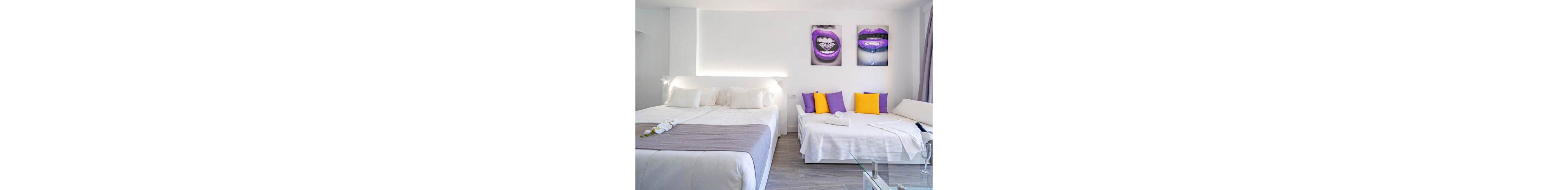 A contemporary hotel room features a large bed and a sofa bed, both dressed in crisp white linens. The space is accented with bright purple and yellow pillows, and two striking wall art pieces depicting lips with purple lipstick. The room is well-lit, with a minimalist design and neutral palette, complemented by glass and wood elements.