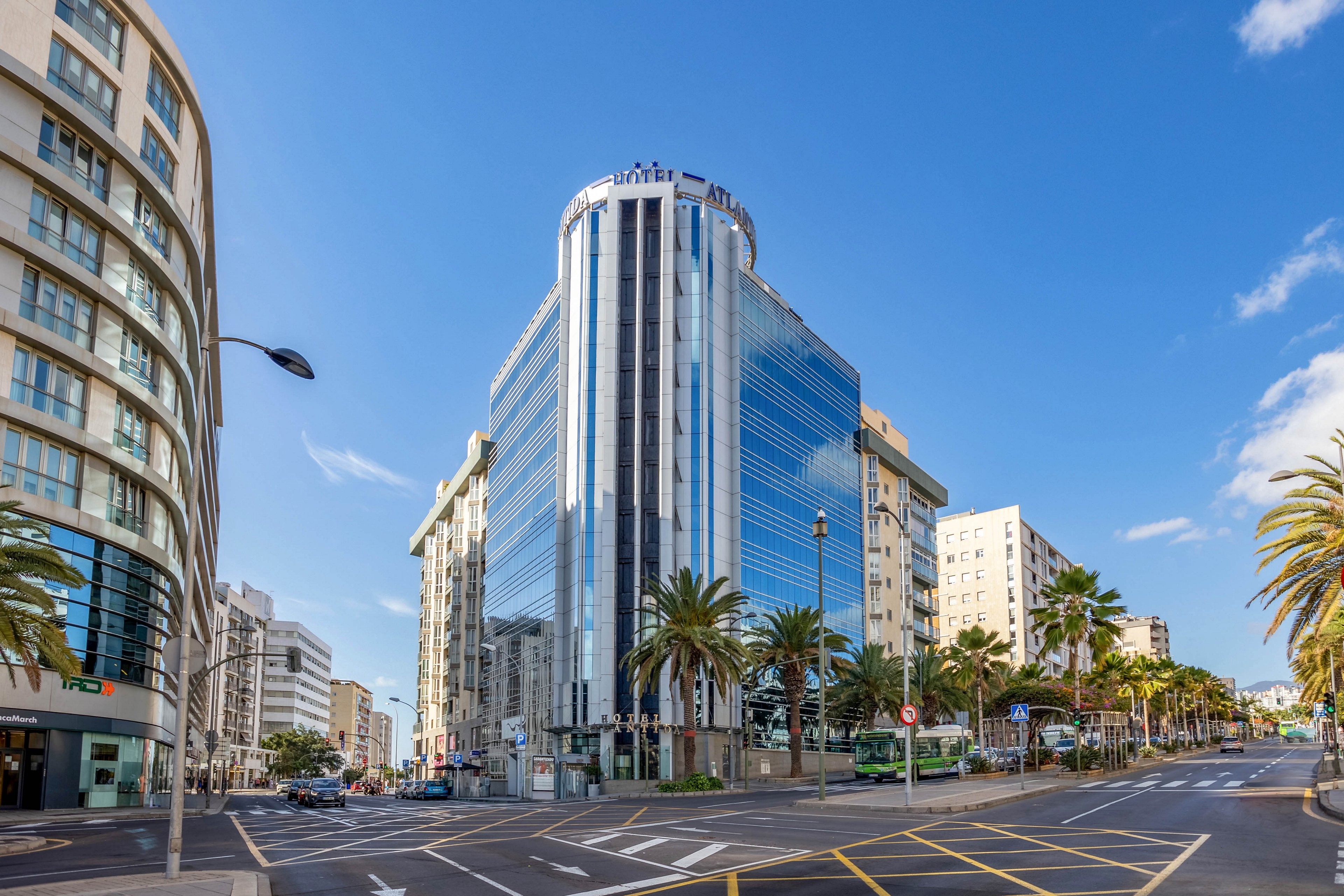 A tall, contemporary office building with reflective glass windows stands prominently at a city intersection. The setting features palm trees, wide streets, and surrounding mid-rise architecture under a clear blue sky. The mood is bright and professional, with clean lines and urban visuals. No visible text or numeric values are present in the image.