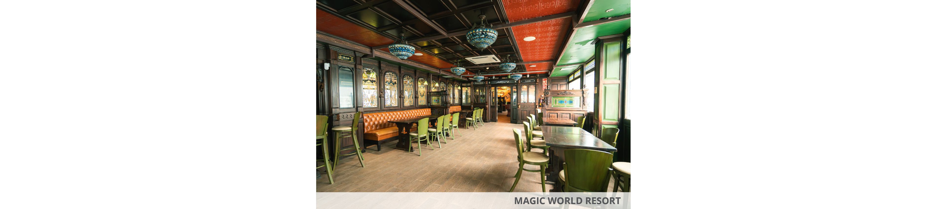 Spacious pub interior features wooden paneling, stained glass windows, and green chairs around large tables. A tufted leather bench lines one wall beneath decorative glass panels, creating a classic bar atmosphere. Colorful hanging lamps and a patterned red ceiling add character to the room. The space is empty of people, highlighting the layout and design details.