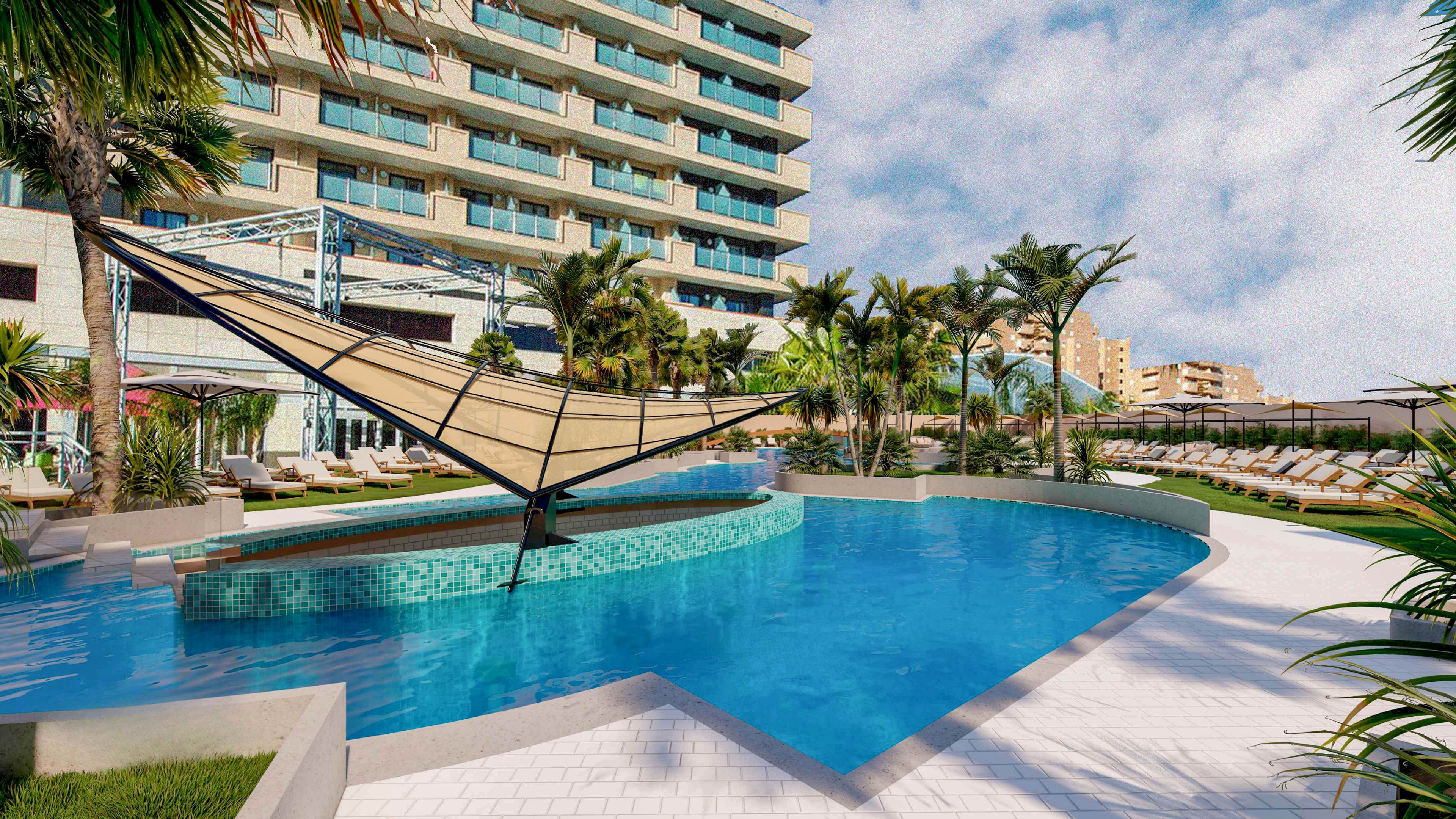A contemporary resort features a large curved swimming pool surrounded by palm trees and sun loungers. A distinctive triangular shade structure rises from a circular tiled platform in the center of the pool. The multi-story hotel building with balconies forms the backdrop under a bright, partly cloudy sky. The scene suggests a relaxing vacation atmosphere with ample seating and open outdoor space.