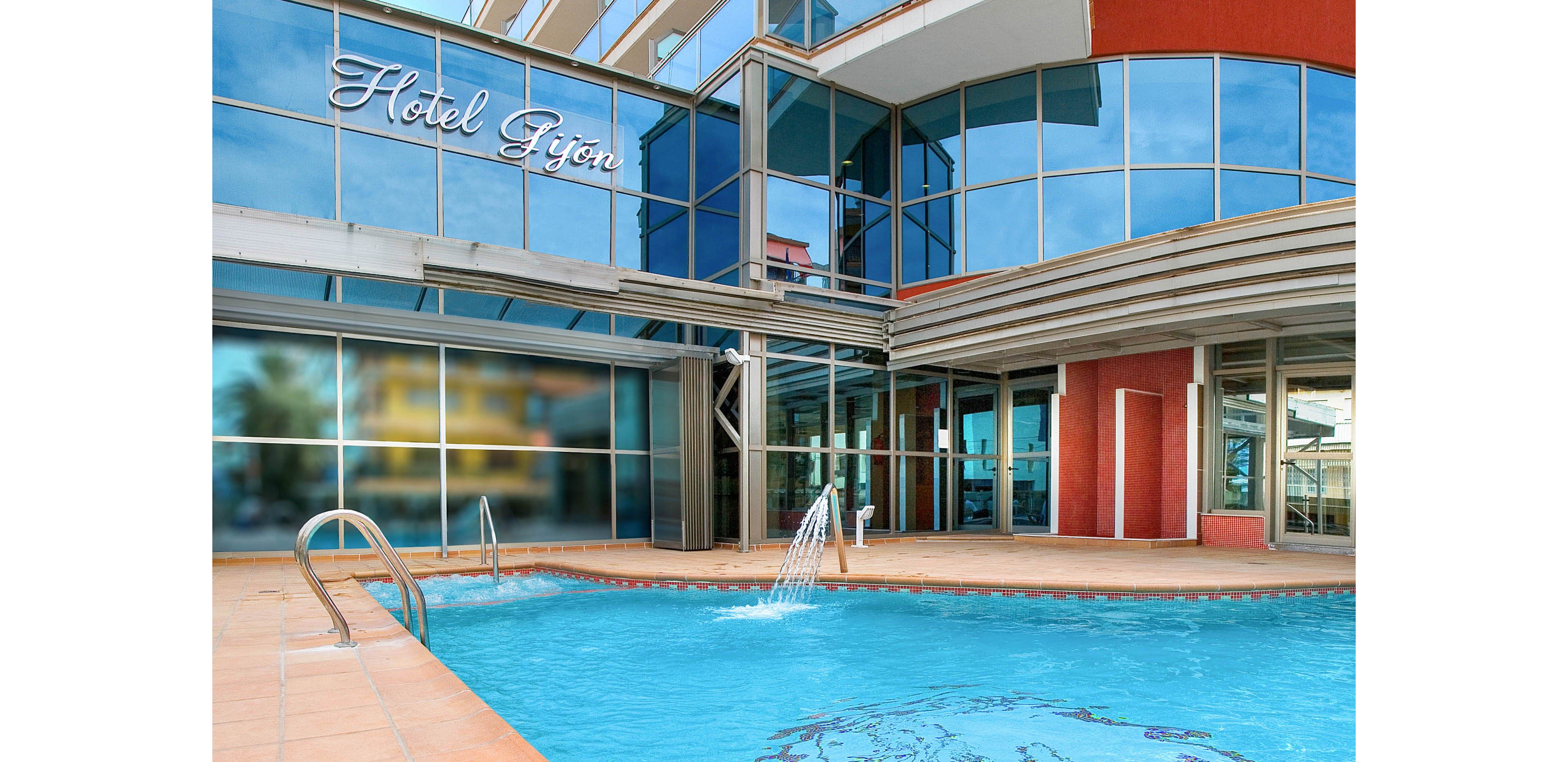 An outdoor swimming pool is situated in front of a modern hotel building with large glass windows. Two adults are enjoying the water, one raising their arms while another relaxes nearby. The pool deck is tiled, and the hotel name "Hotel Gijon" is clearly visible on the facade. Bright daylight and clear blue water create a refreshing vacation atmosphere.