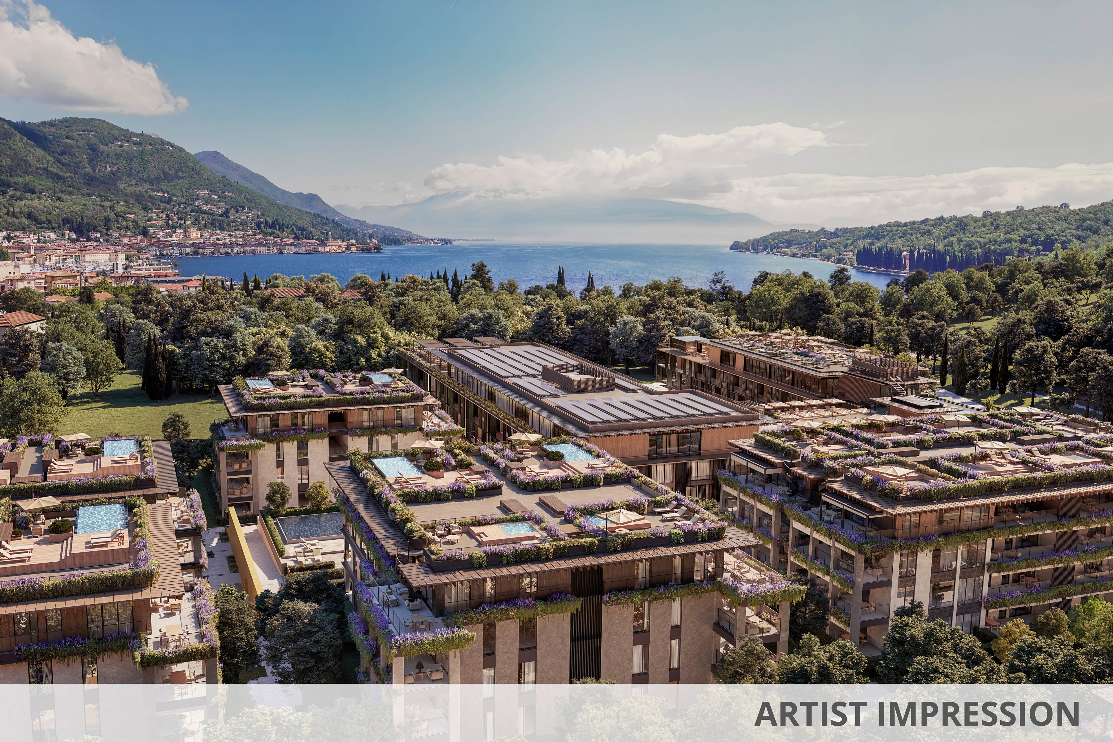 Aerial view of a contemporary residential complex with rooftop gardens and swimming pools, set amidst lush greenery. The buildings are situated near a large, tranquil lake with mountains and a small town visible in the background. The scene is bathed in natural daylight, highlighting the modern architecture and serene environment. No visible text or numbers are present in the image.
