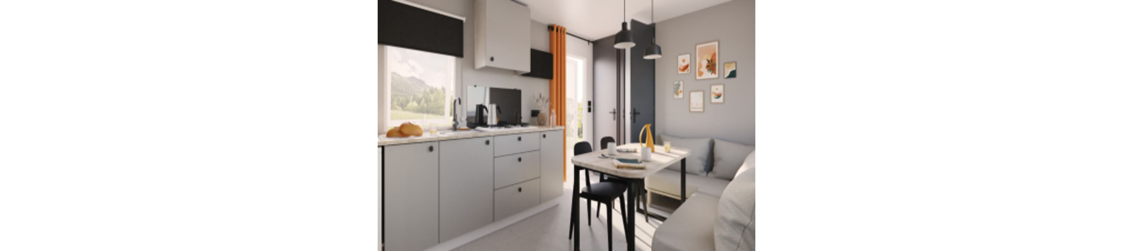 A compact modern kitchen opens into a small dining and living area. Light gray cabinets and countertops are paired with black accents and simple appliances. A table with black chairs sits beside a soft sofa, with framed artwork decorating the wall. Natural light streams in through the window and glass door, creating a bright, inviting atmosphere.
